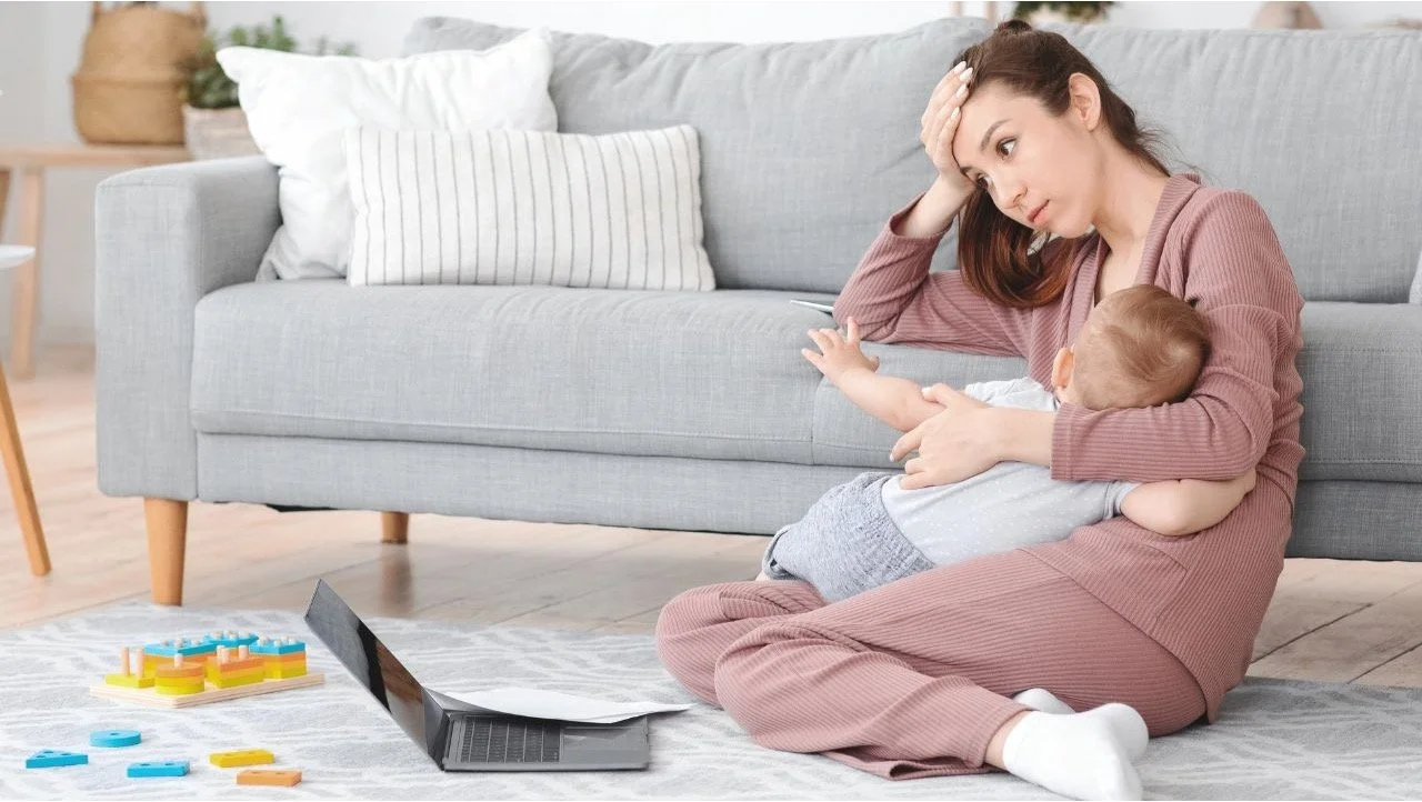 stressed woman looking at laptop while holding baby