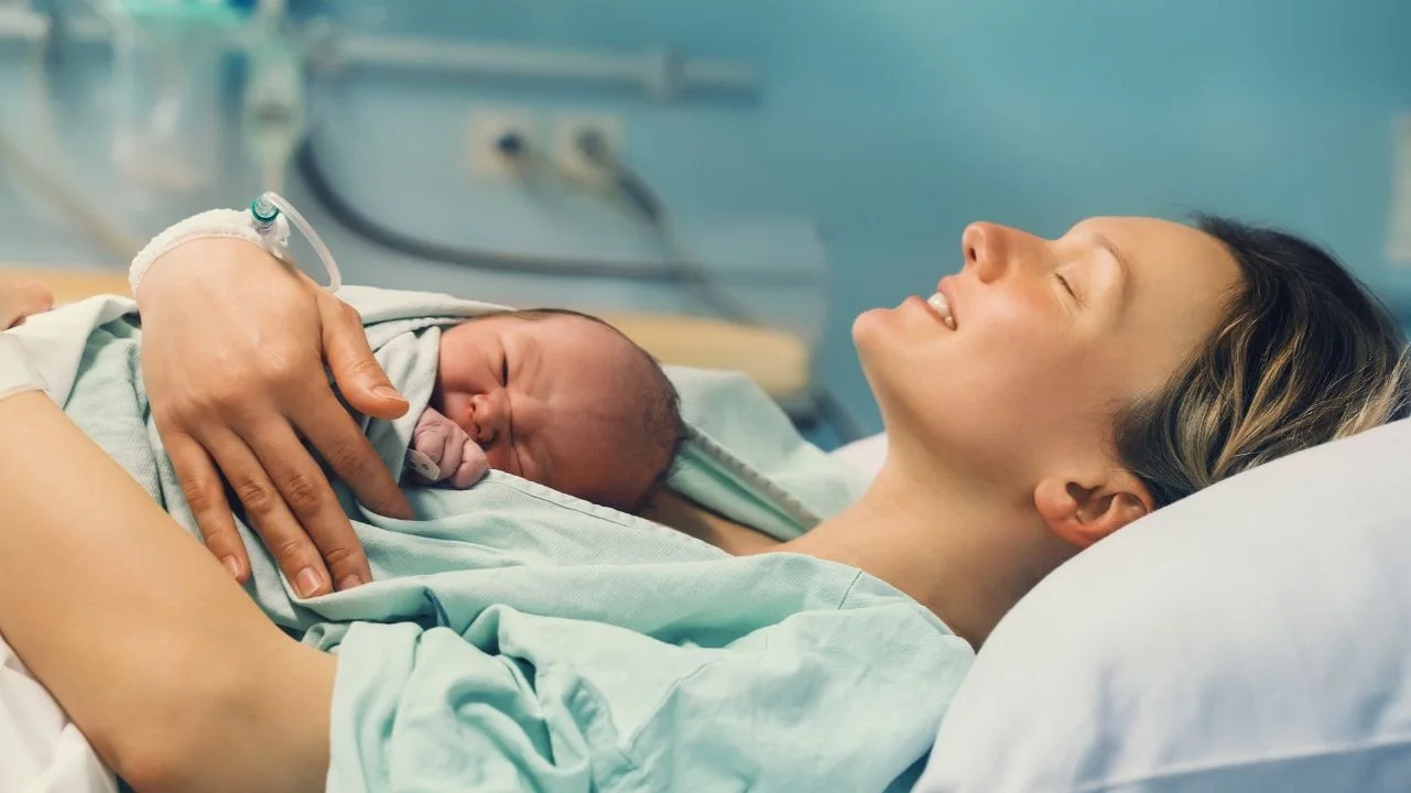 woman smiling holding baby after giving birth in hospital
