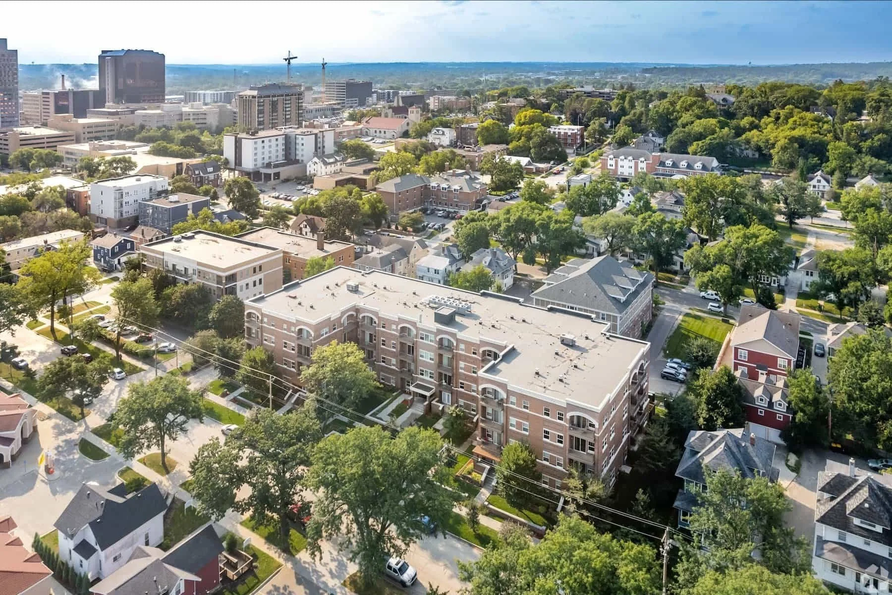 Aerial view of apartments in Rochester, houses, and trees in a vibrant residential neighborhood on a sunny day.