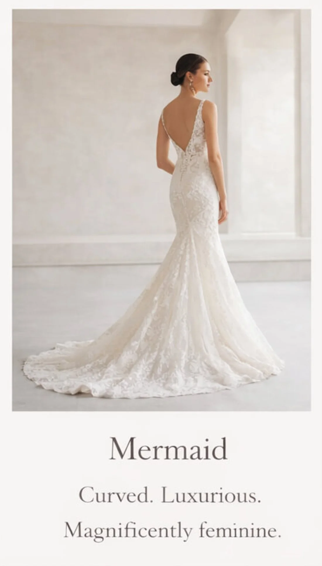 A bride in a white, lace, mermaid-style wedding gown with a deep V back, standing in a minimalistic, bright room.