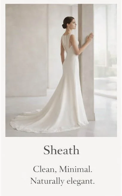 A woman in a white, sleeveless wedding dress with a long train, standing by a window with her hand touching the wall, in a bright, minimalist room.