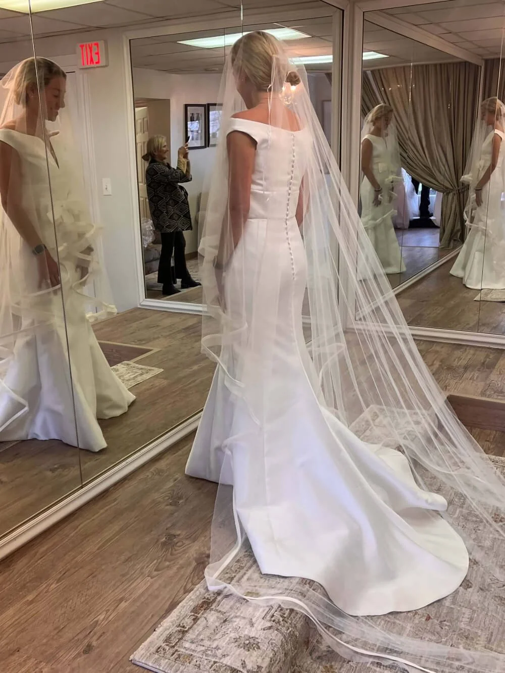 Ashley and Alexandria's bride see herself in a fabulous wedding dress of the showroom as Mom looks on and take a photograph surrounded by family