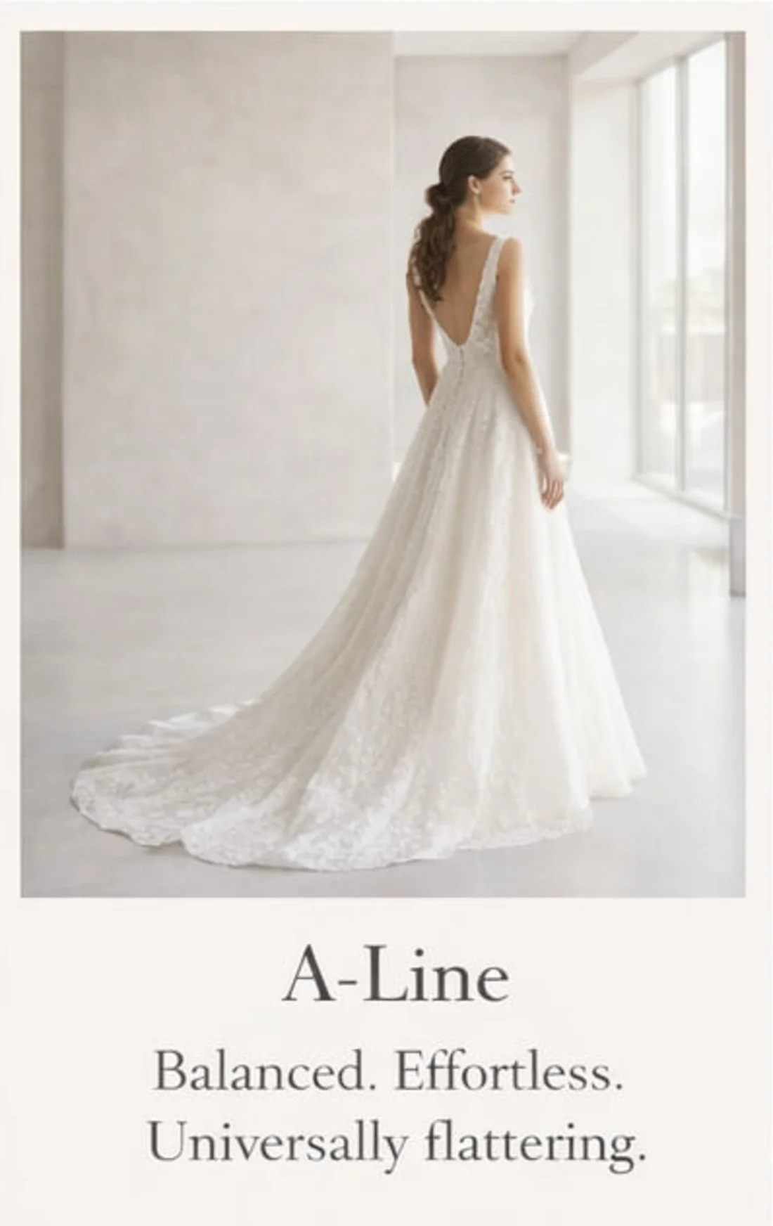 A woman wearing an elegant white wedding dress with a long train, standing indoors near large windows, looking to the side.