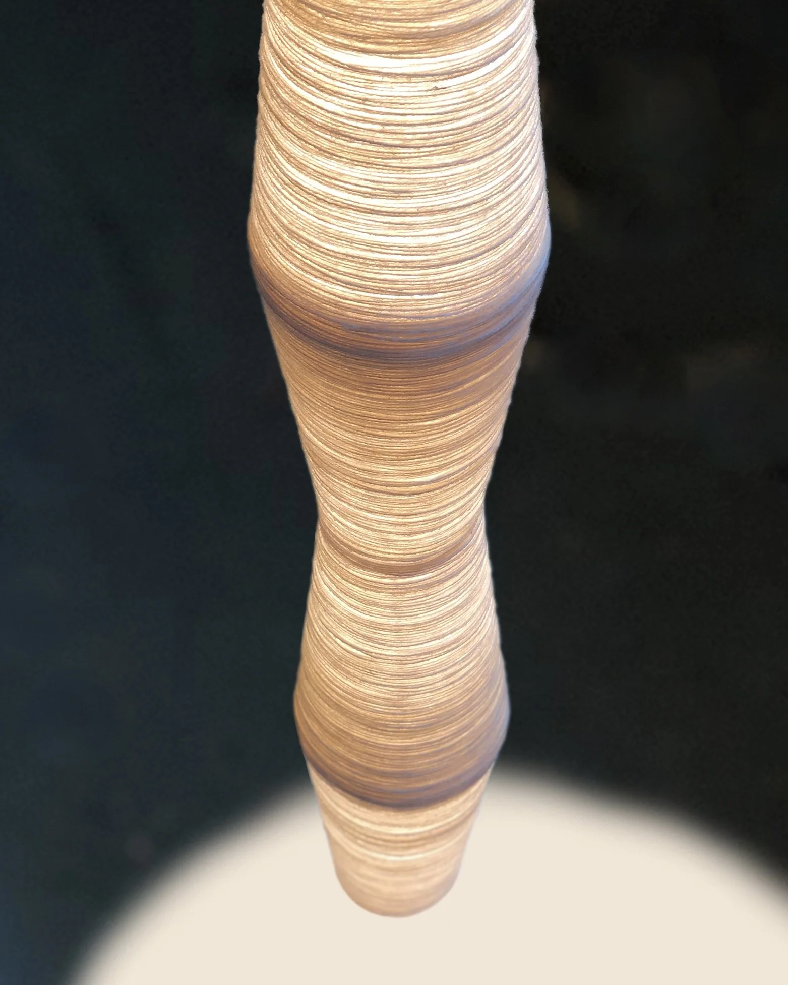 Close-up of a tall, cone-shaped pendant light made of layered, spun wool, set against a dark background.