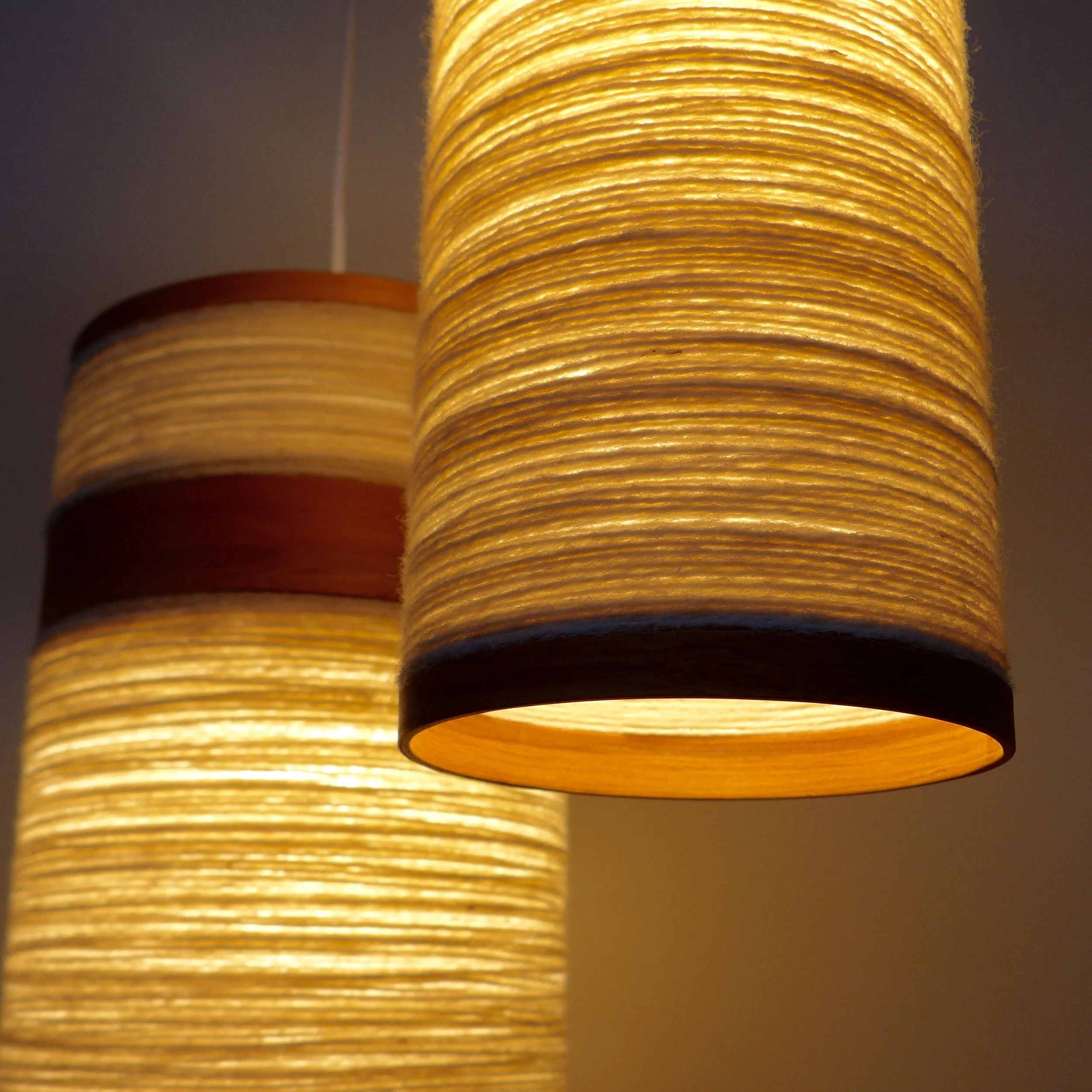 Close-up of three glowing cylindrical lamps with warm yellow light, mounted on the ceiling with visible cords, against a dark background.