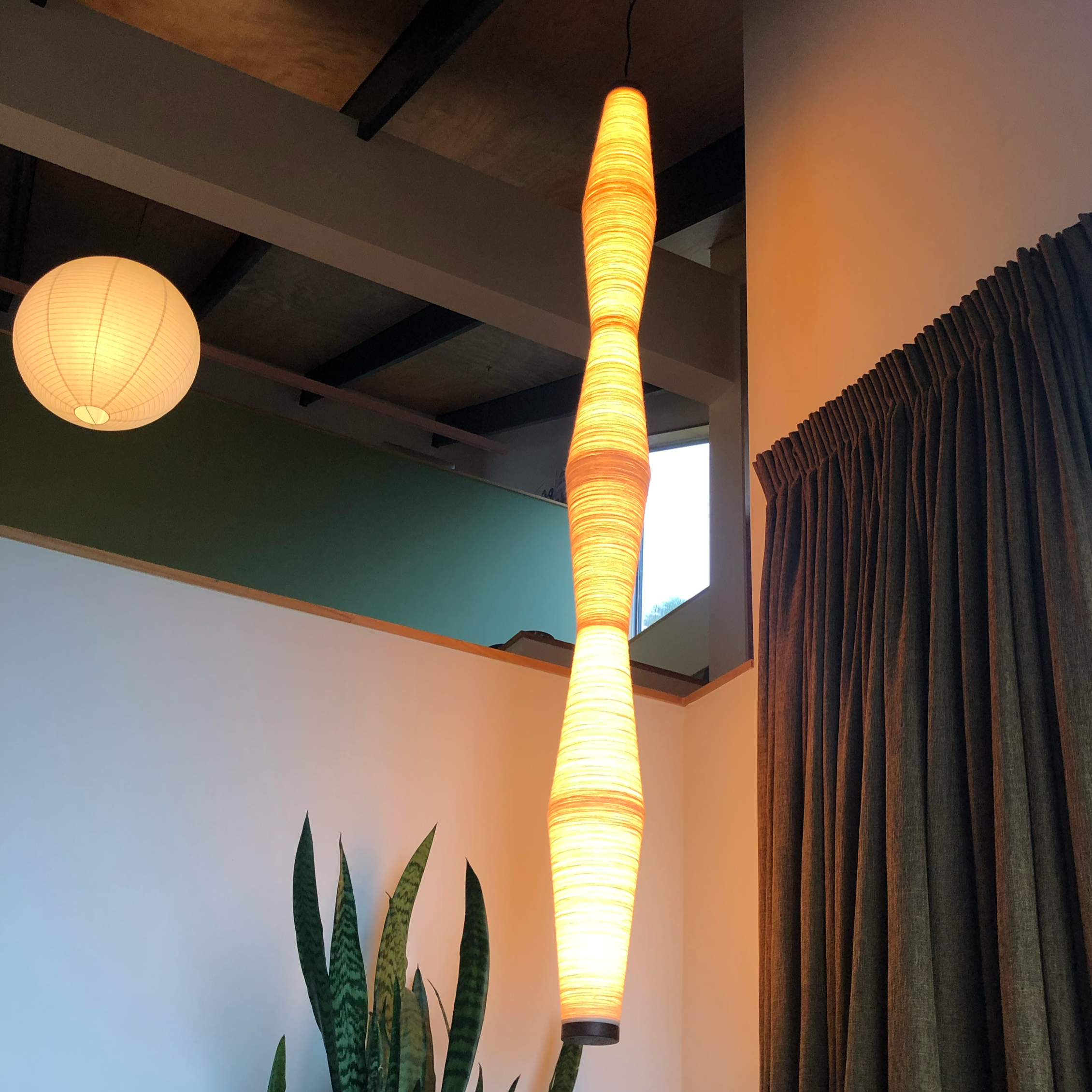 Image of three hanging light fixtures in a room with wooden ceiling beams and green and white walls, along with a plant in the foreground.