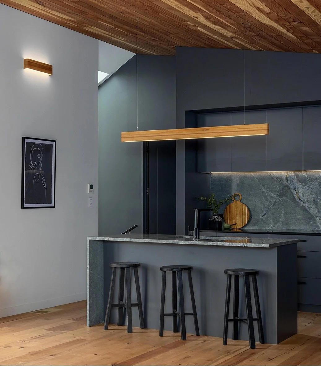 Modern kitchen with dark gray cabinets, a marble island with three black stools, a wooden ceiling, and minimalist decor.