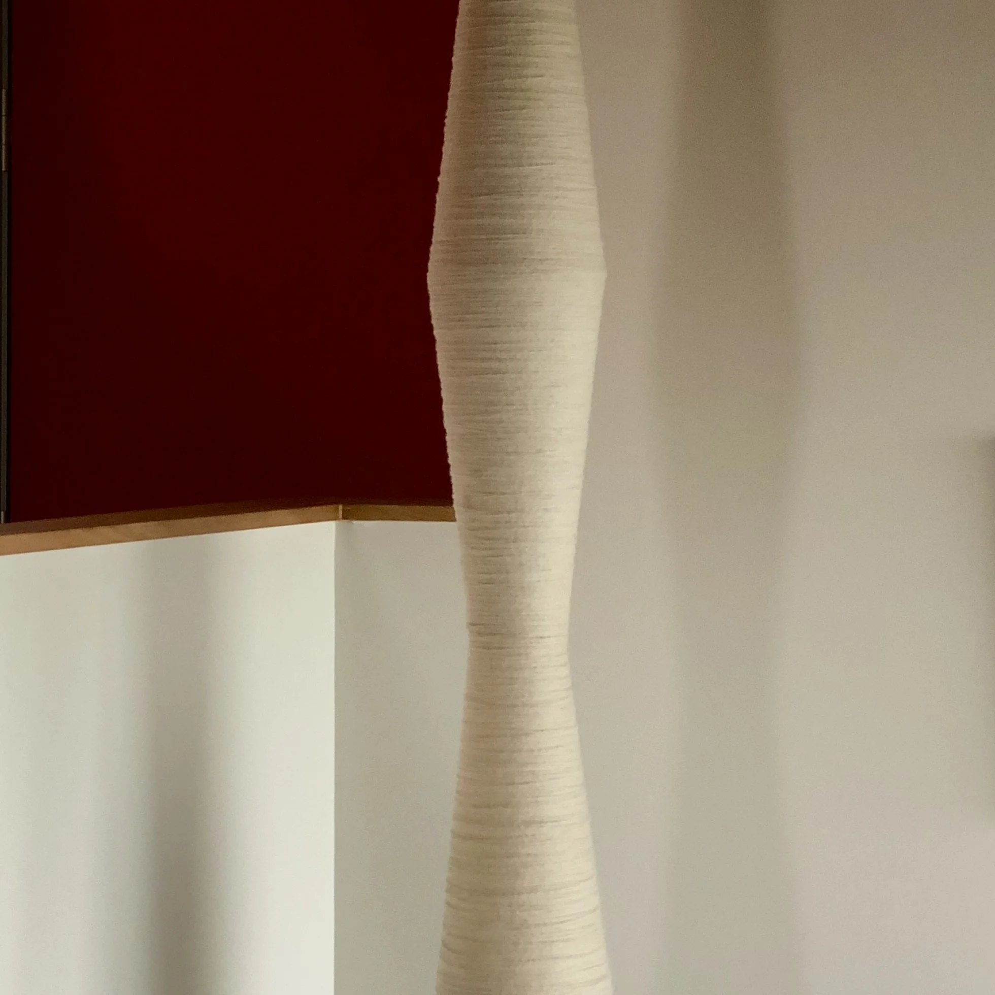 Close-up photo of a sculptural pendant light on a white surface, with a red wall in the background.