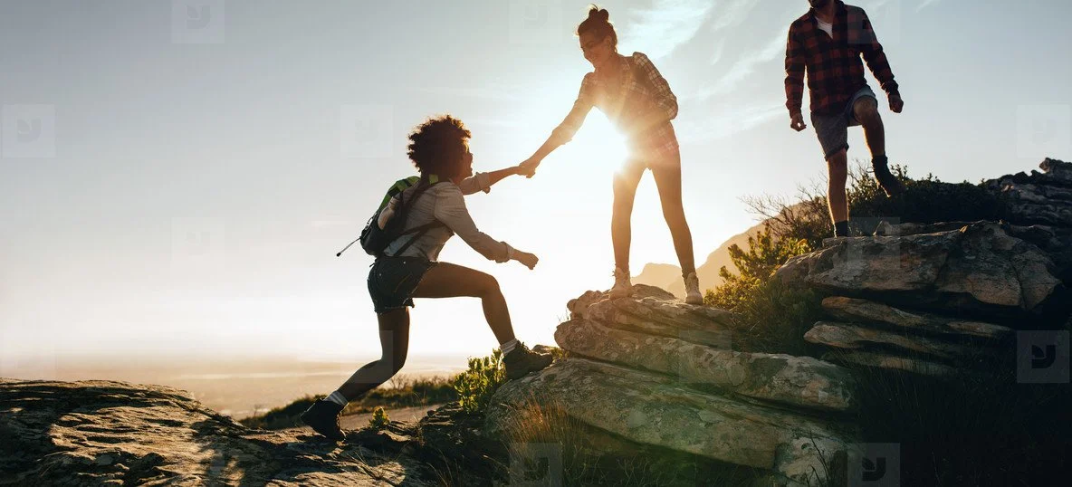 Women climbing and helping each other up at sunset.