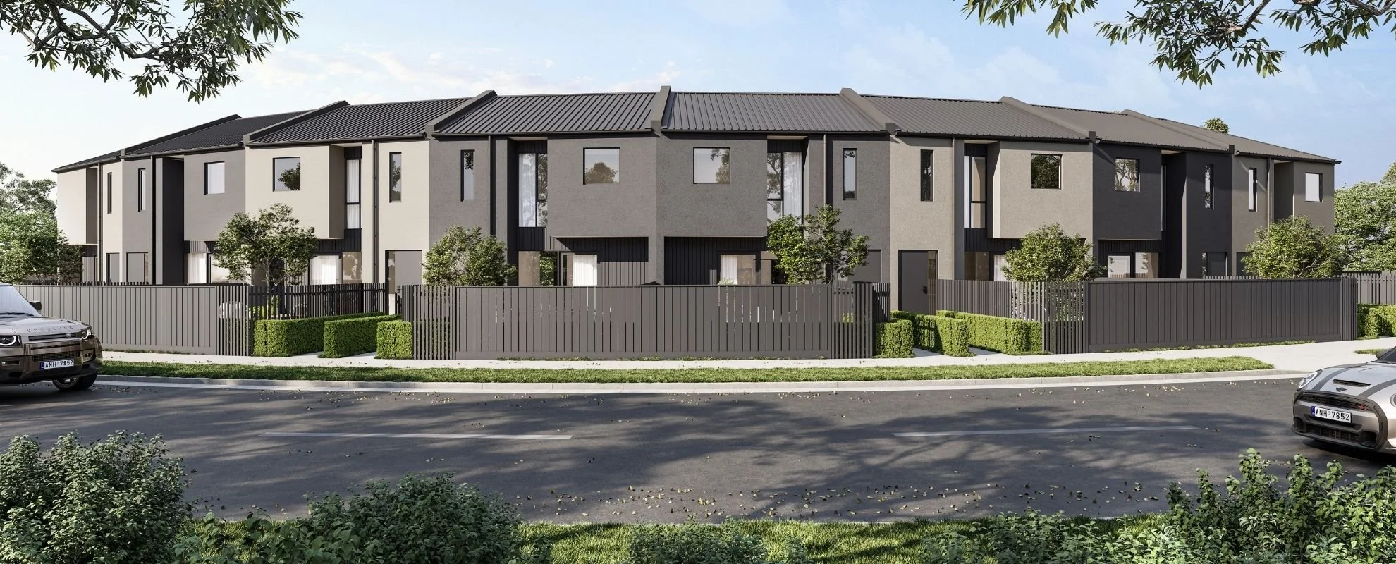 A modern residential complex with multiple townhouses behind a black fence, surrounded by landscaped greenery and parked cars on a street.