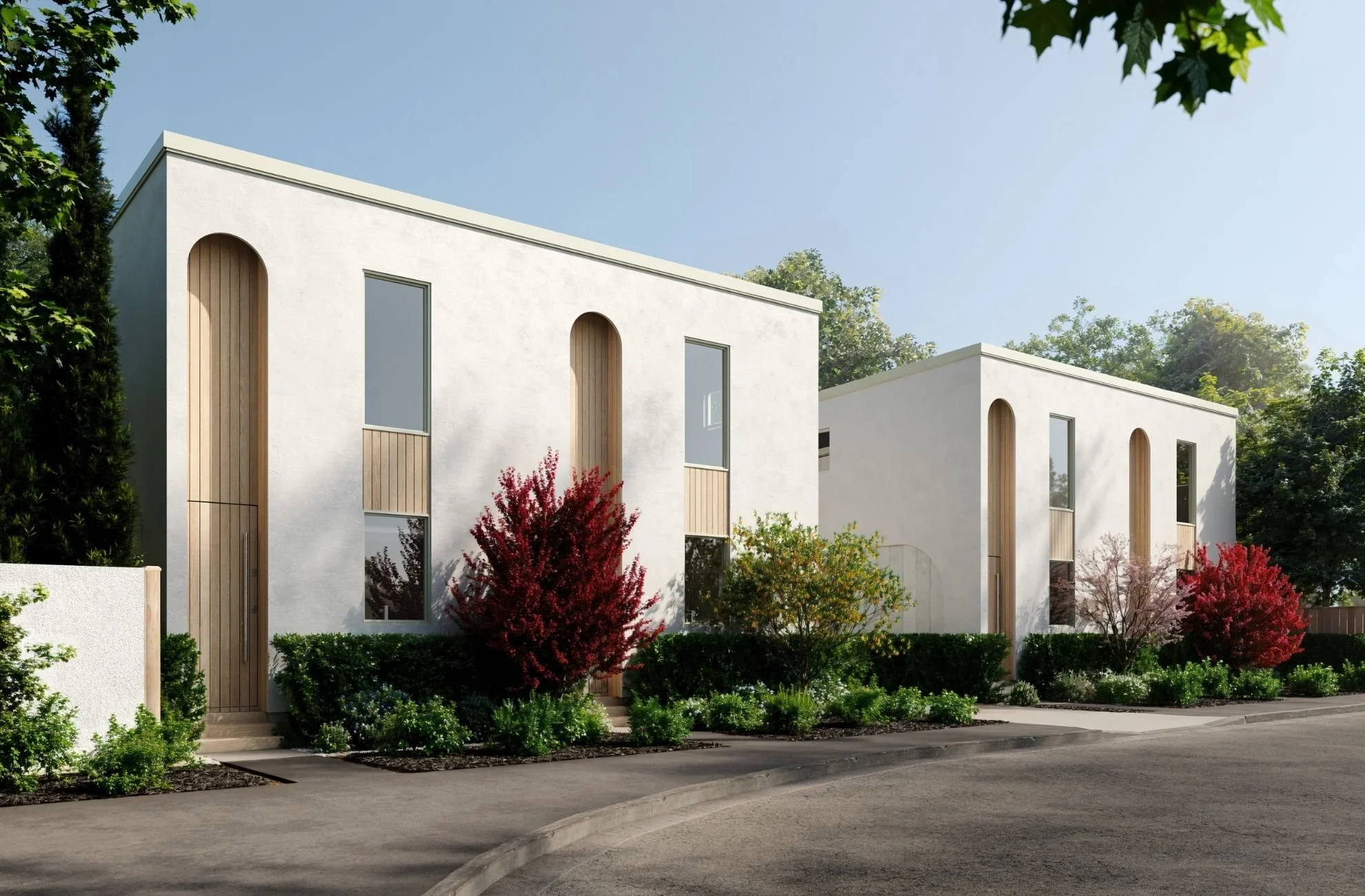 Modern white residential buildings with tall arched windows, wooden accents, surrounded by landscaped greenery and colorful shrubs, under a clear blue sky.