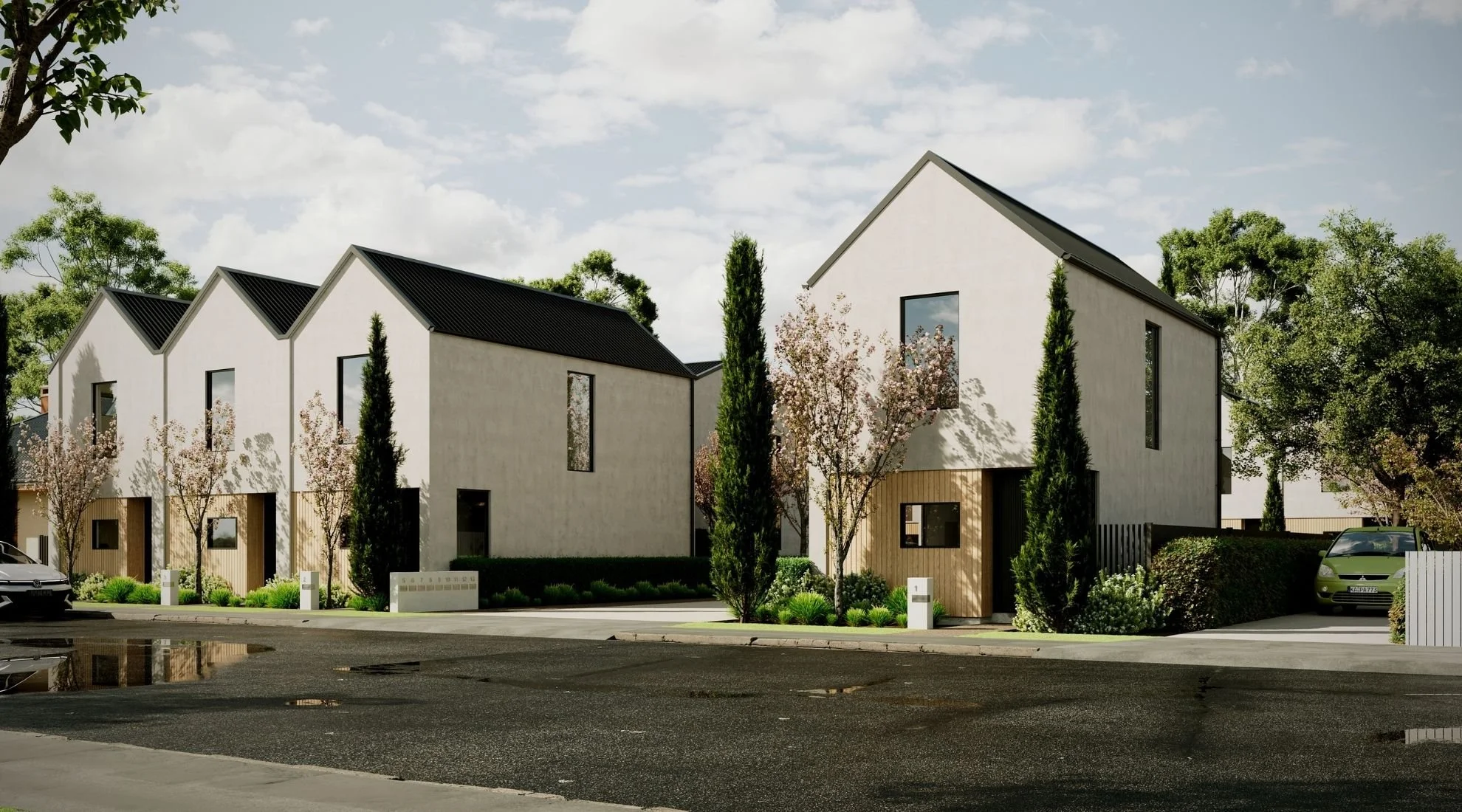 Modern residential buildings with sloped roofs, surrounded by trees and greenery, under a partly cloudy sky.
