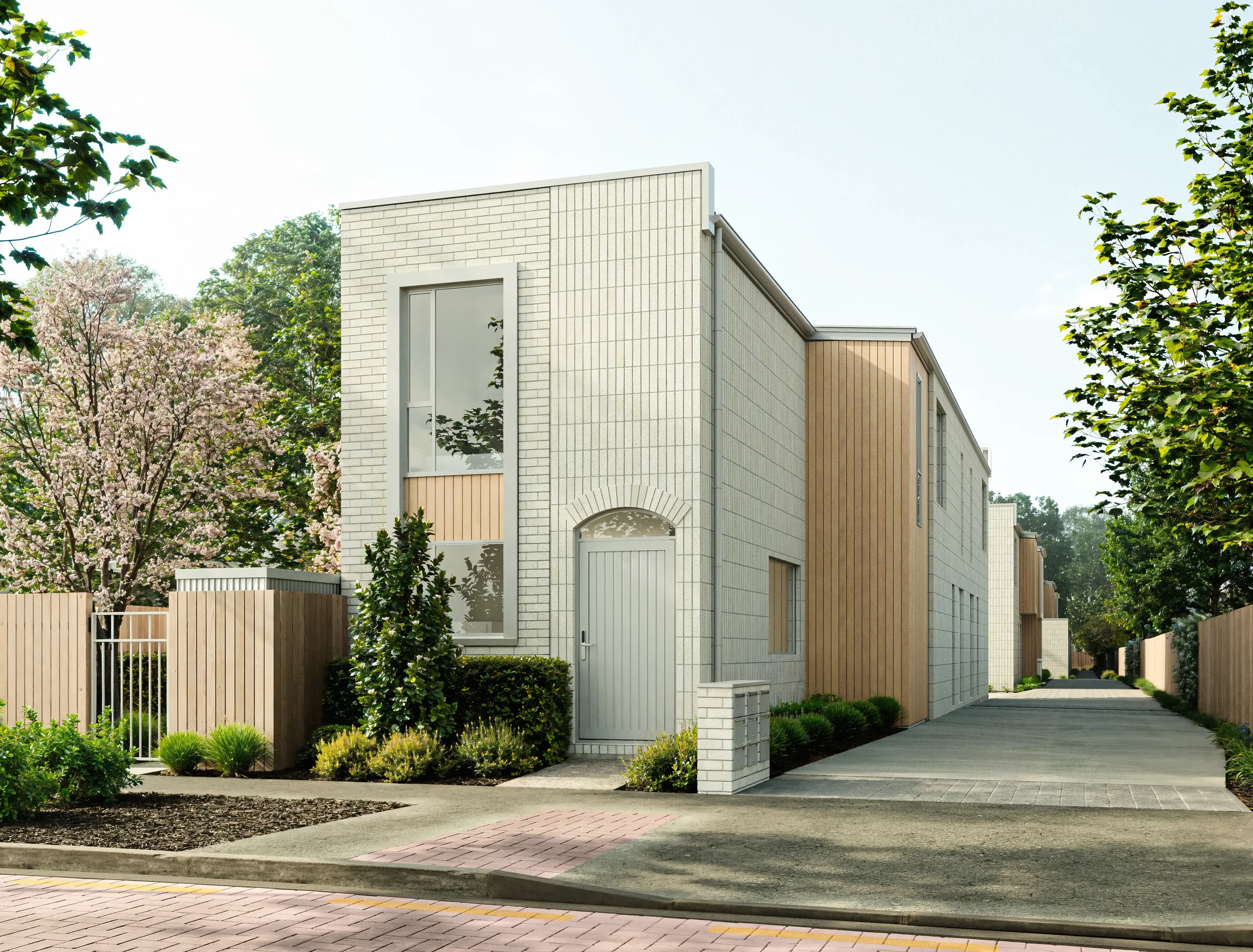 Modern white and wood-paneled multi-family residential building with landscaped front yard and driveway, trees, and clear sky.