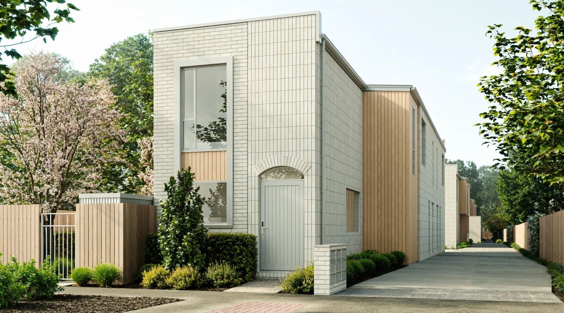 A modern residential building with white brick and wooden panel exterior, large windows, a white door, and a small front garden with shrubs, surrounded by a paved driveway and greenery.