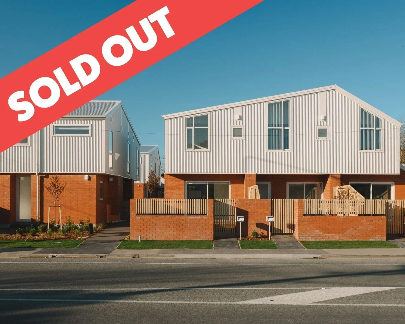 Modern two-story house with white upper level, brick lower level, black fencing, trees, and a driveway, marked as sold out.