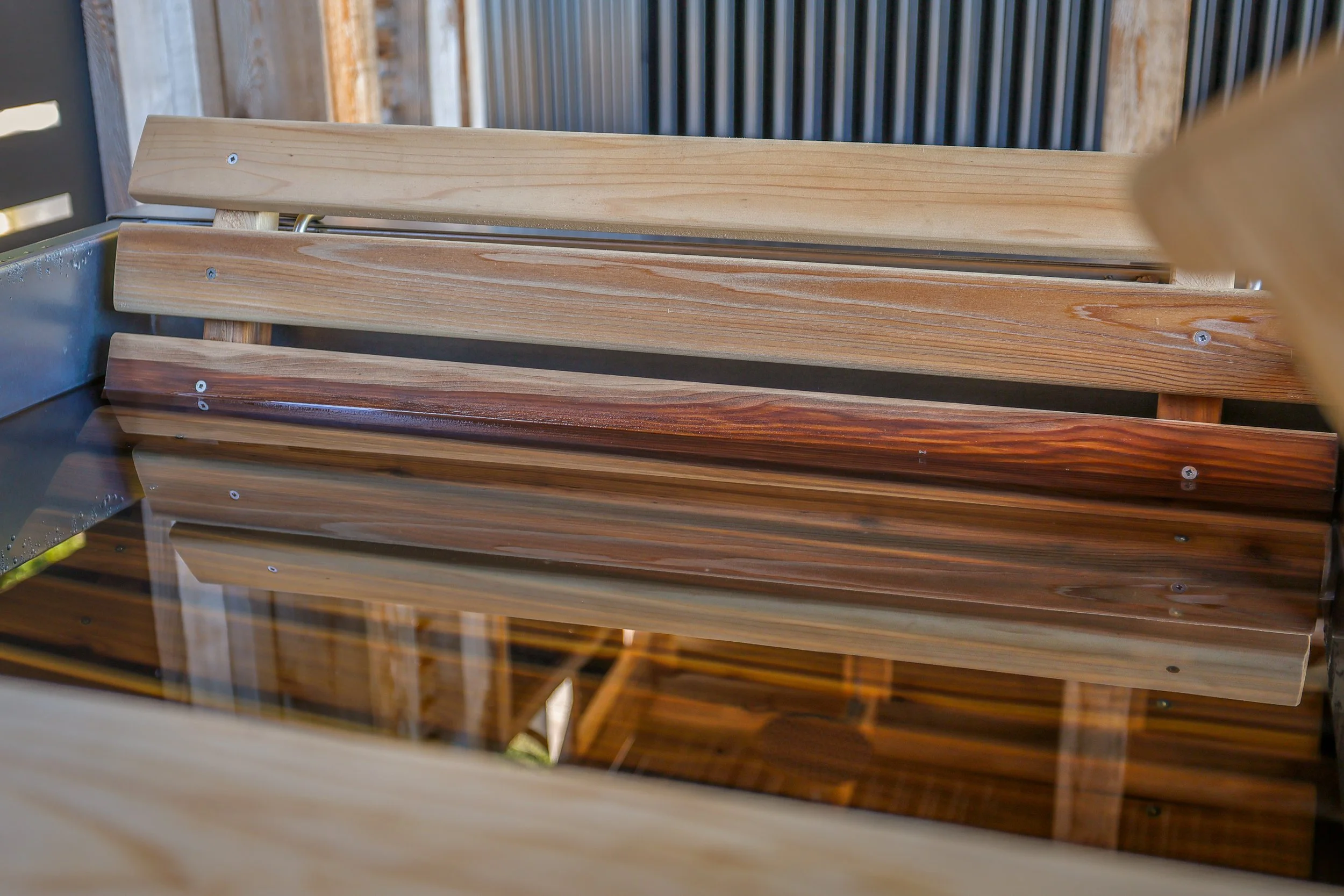 Stacked wooden planks and a glass surface reflecting the wood.