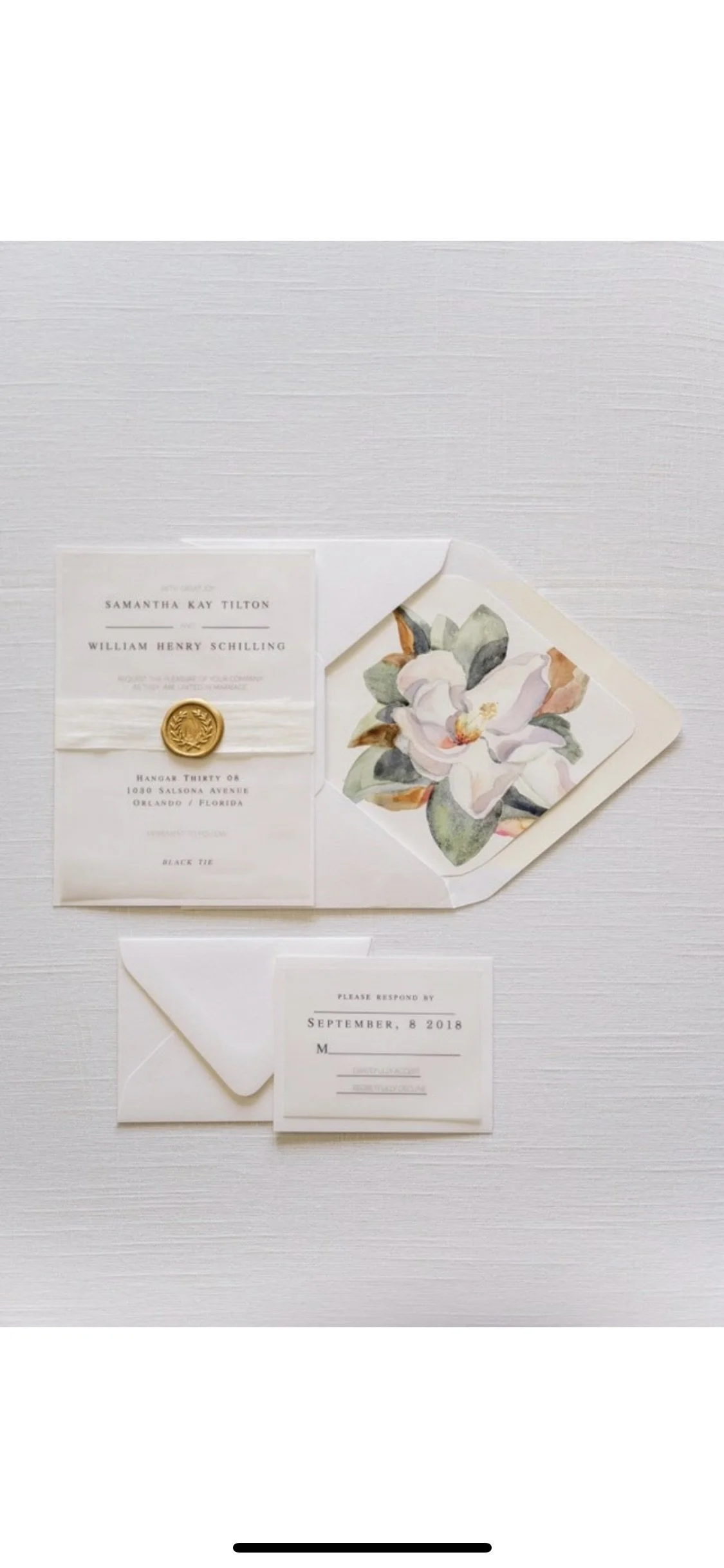 luxury wedding invitation suite with black thermography printed on vellum stock, wrapped in white silk ribbon and sealed with a gold wax seal. Watercolor magnolia envelope liner puts the finishing touch on this beautiful suite