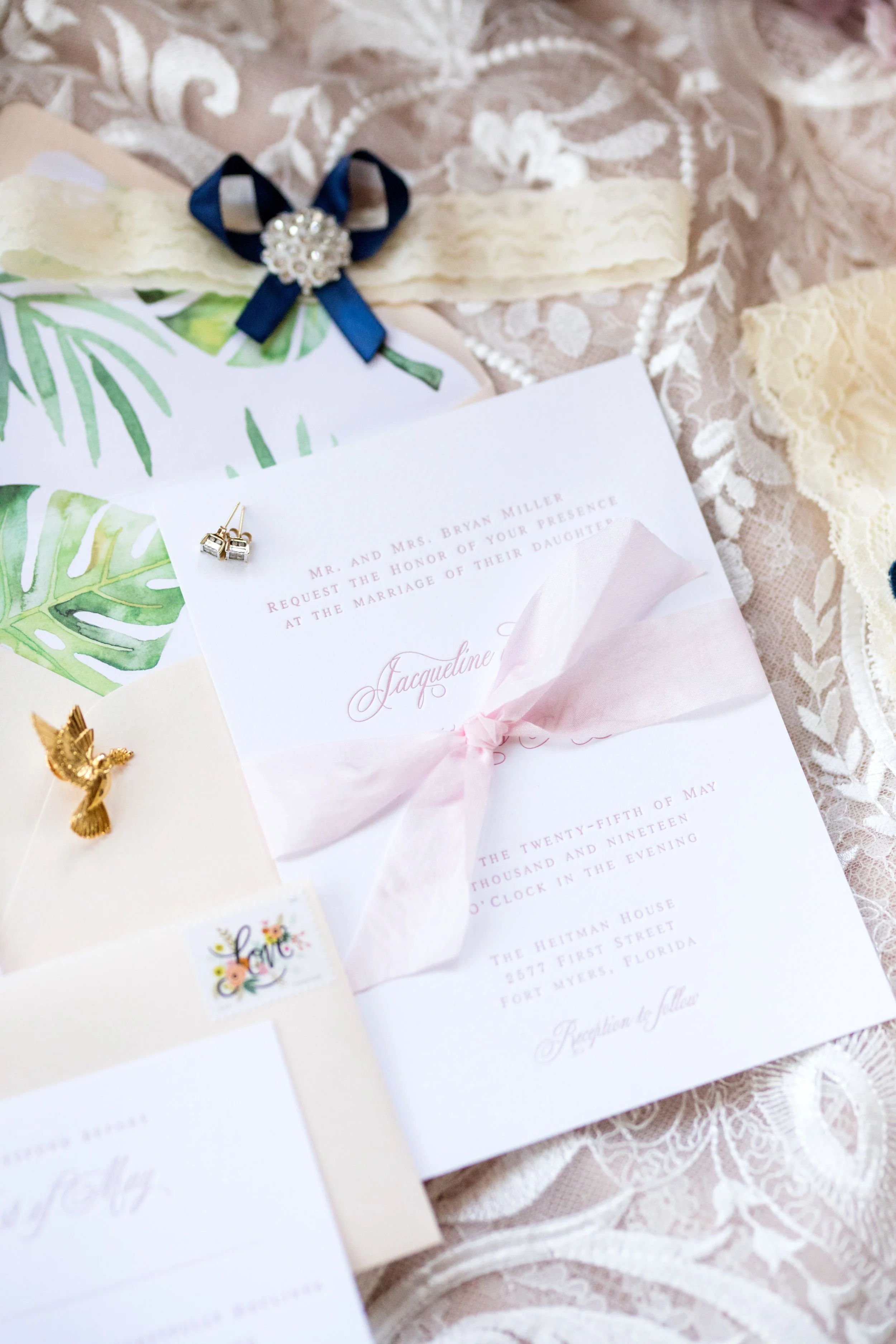 Jacqueline luxury wedding invitation suite featuring pink letterpress, pink silk ribbon, blush envelope with watercolor monstera envelope liner. Handmade paper vow book, velvet pink ring box, monogram garter and pink satin shoes