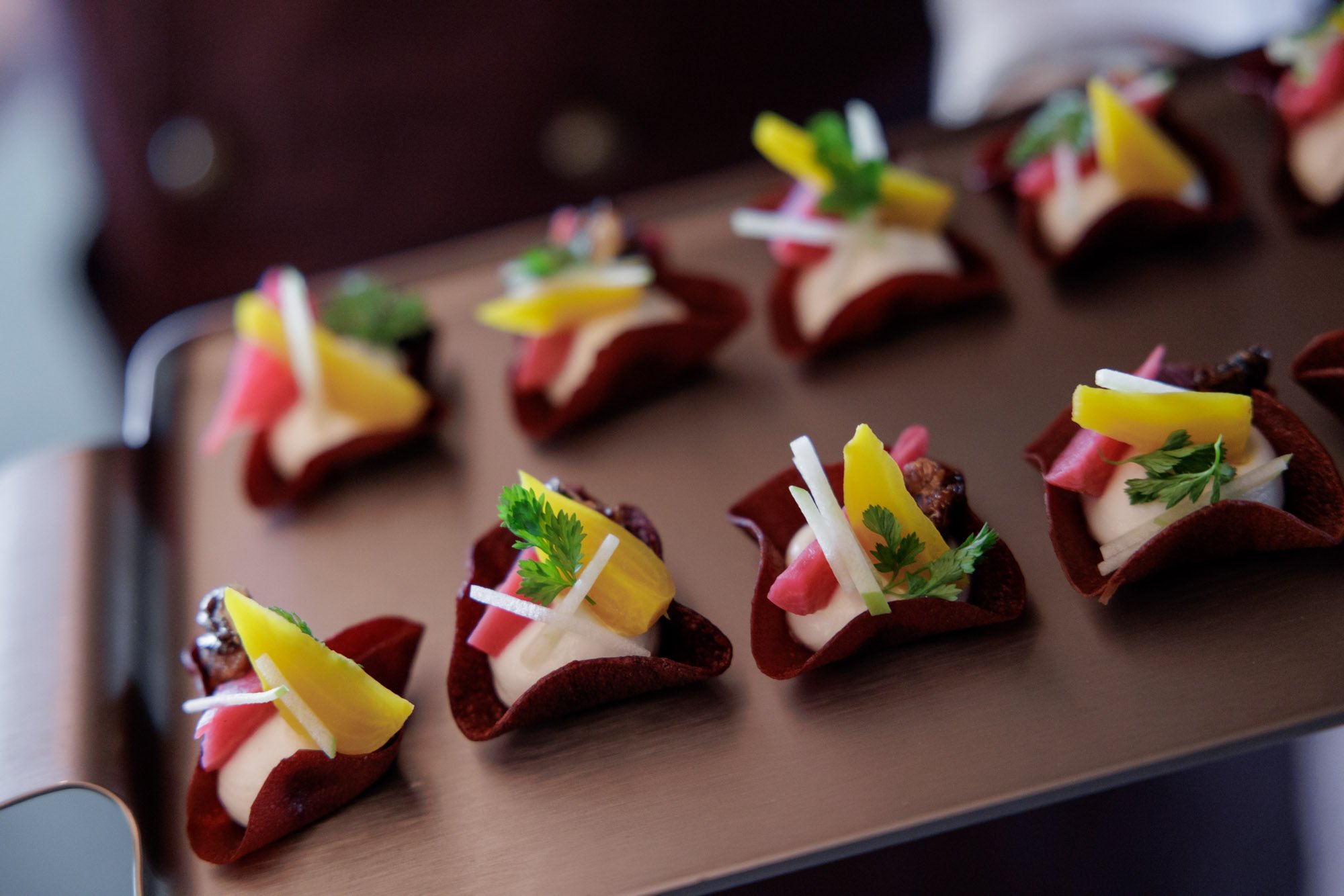 Appetizers with tortilla cups filled with cream, topped with herbs, vegetables, and garnishes on a tray.
