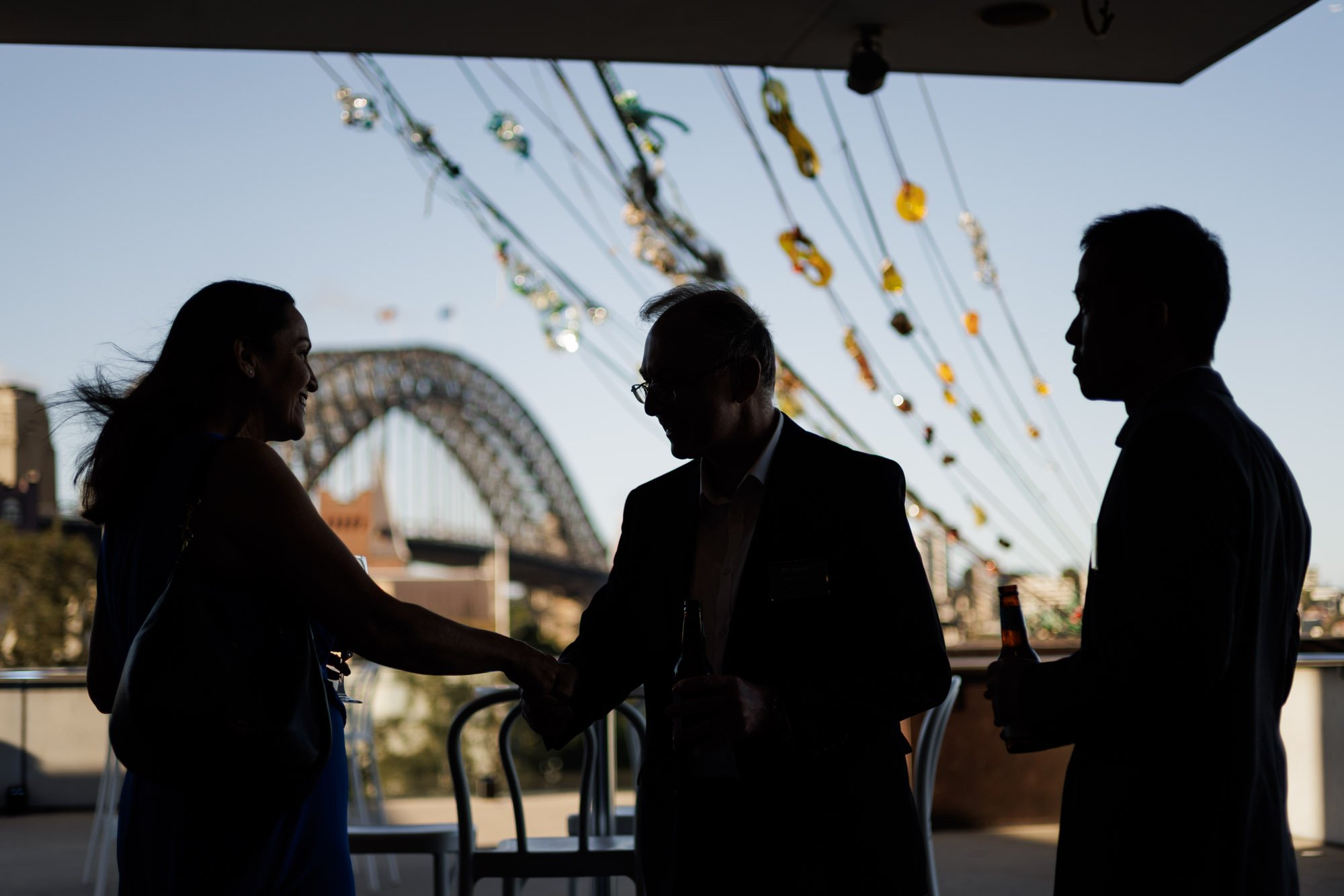 Silhouettes of three people socializing on a balcony with a Ferris wheel in the background.