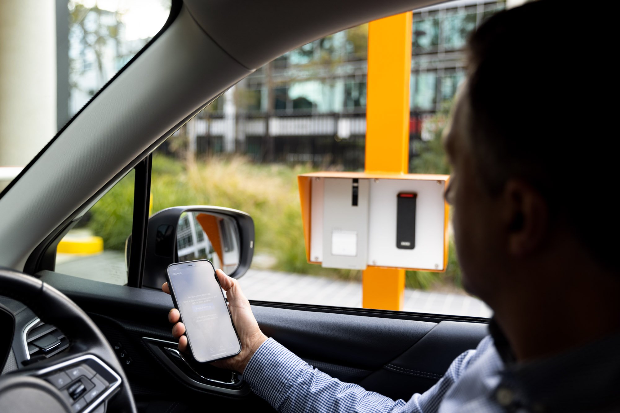 A man sitting in a car near a toll booth using a smartphone.