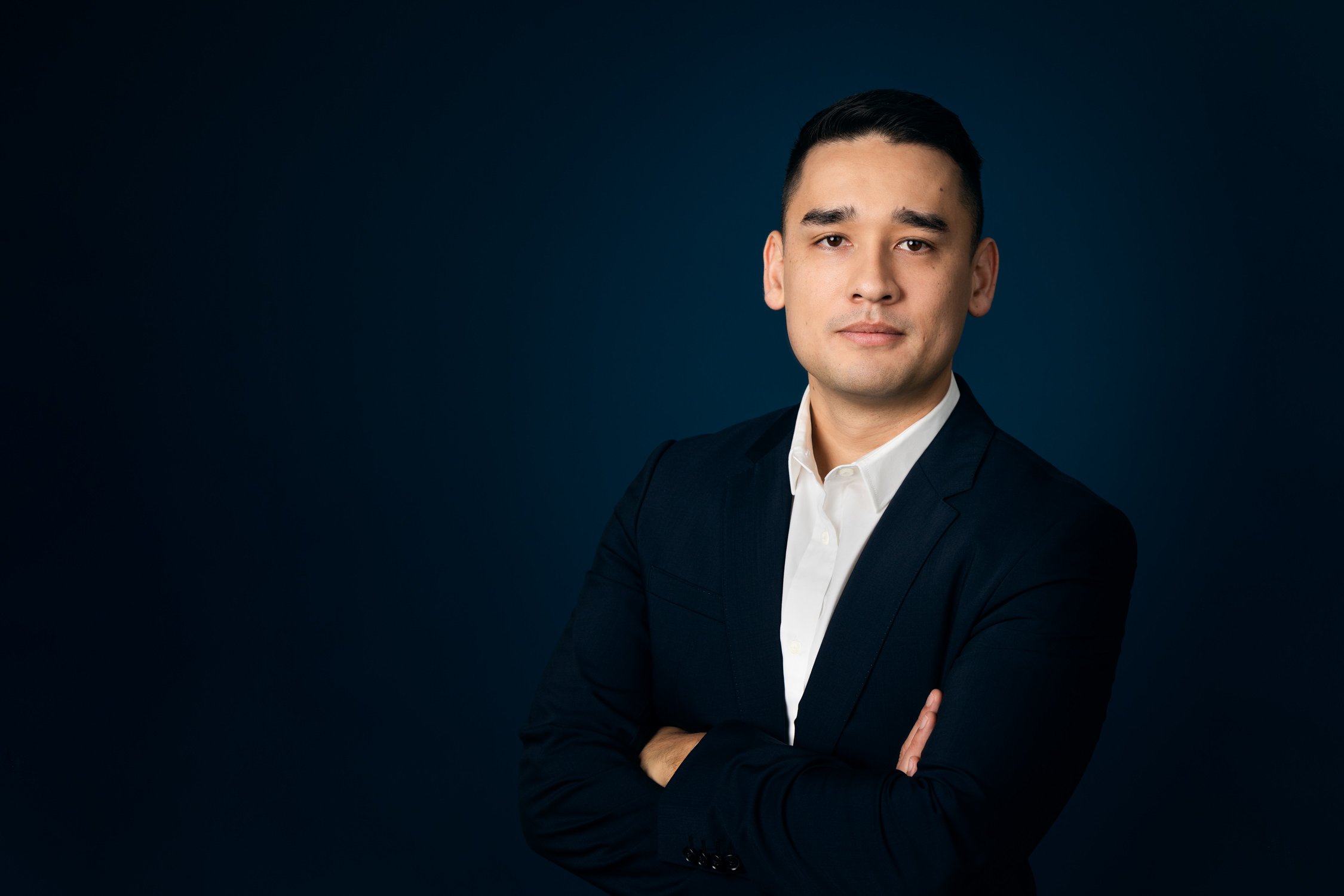 Professional corporate headshot photography for Sydney man in a dark suit with crossed arms against a dark background.