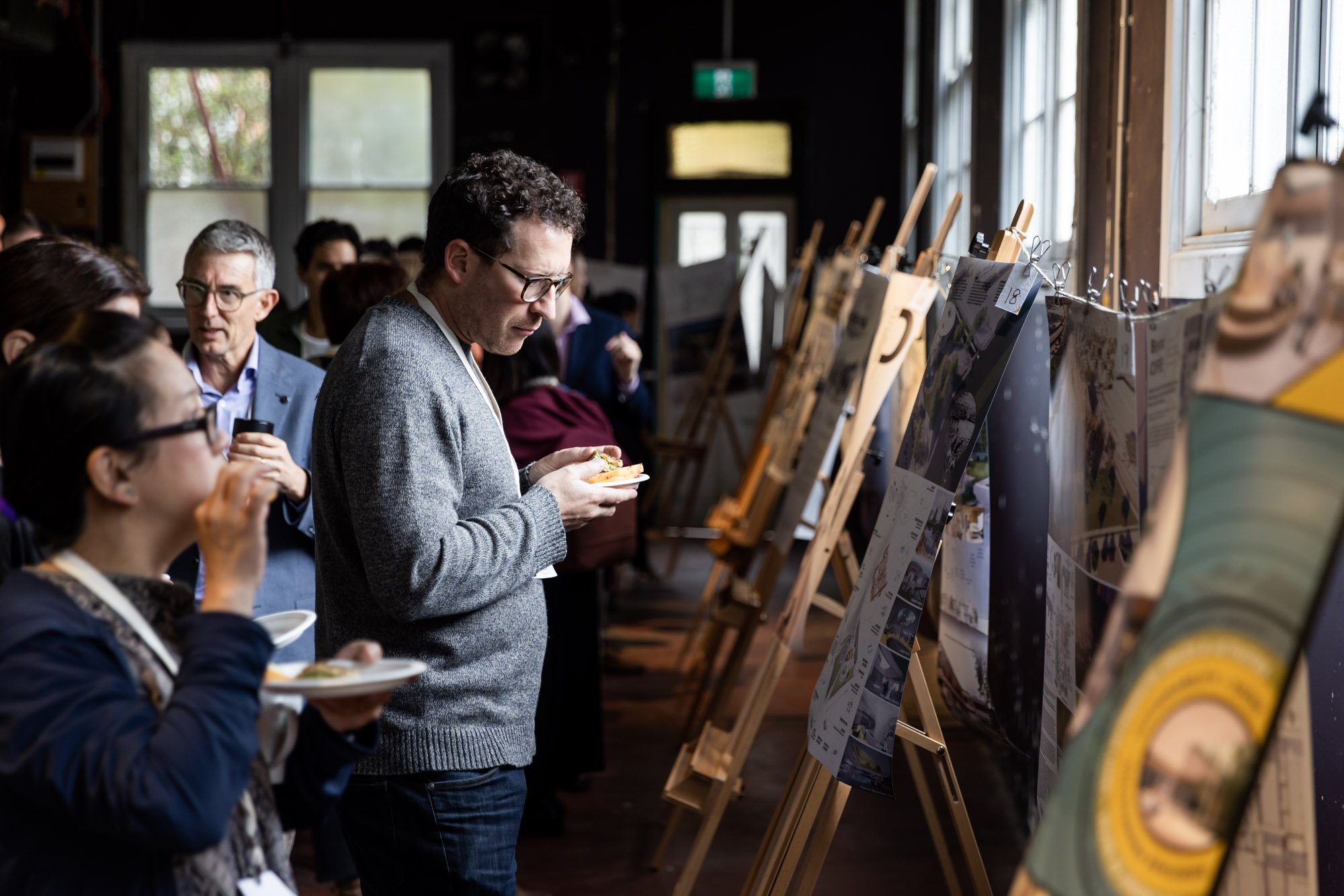People viewing artwork displayed on easels at an indoor art exhibit.