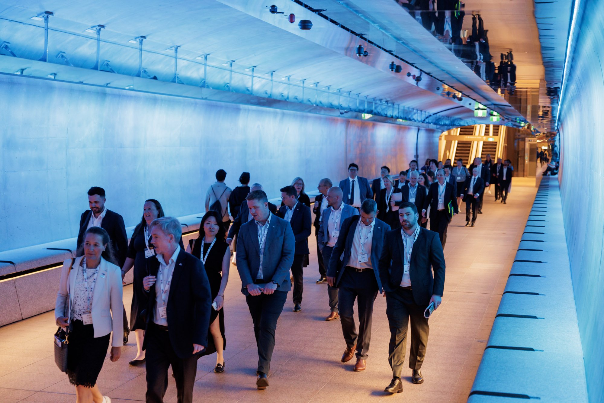 Business professionals walking through a modern, brightly lit corridor at a conference or corporate event.
