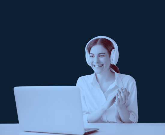 A woman with headphones smiling and clapping while sitting in front of a laptop.