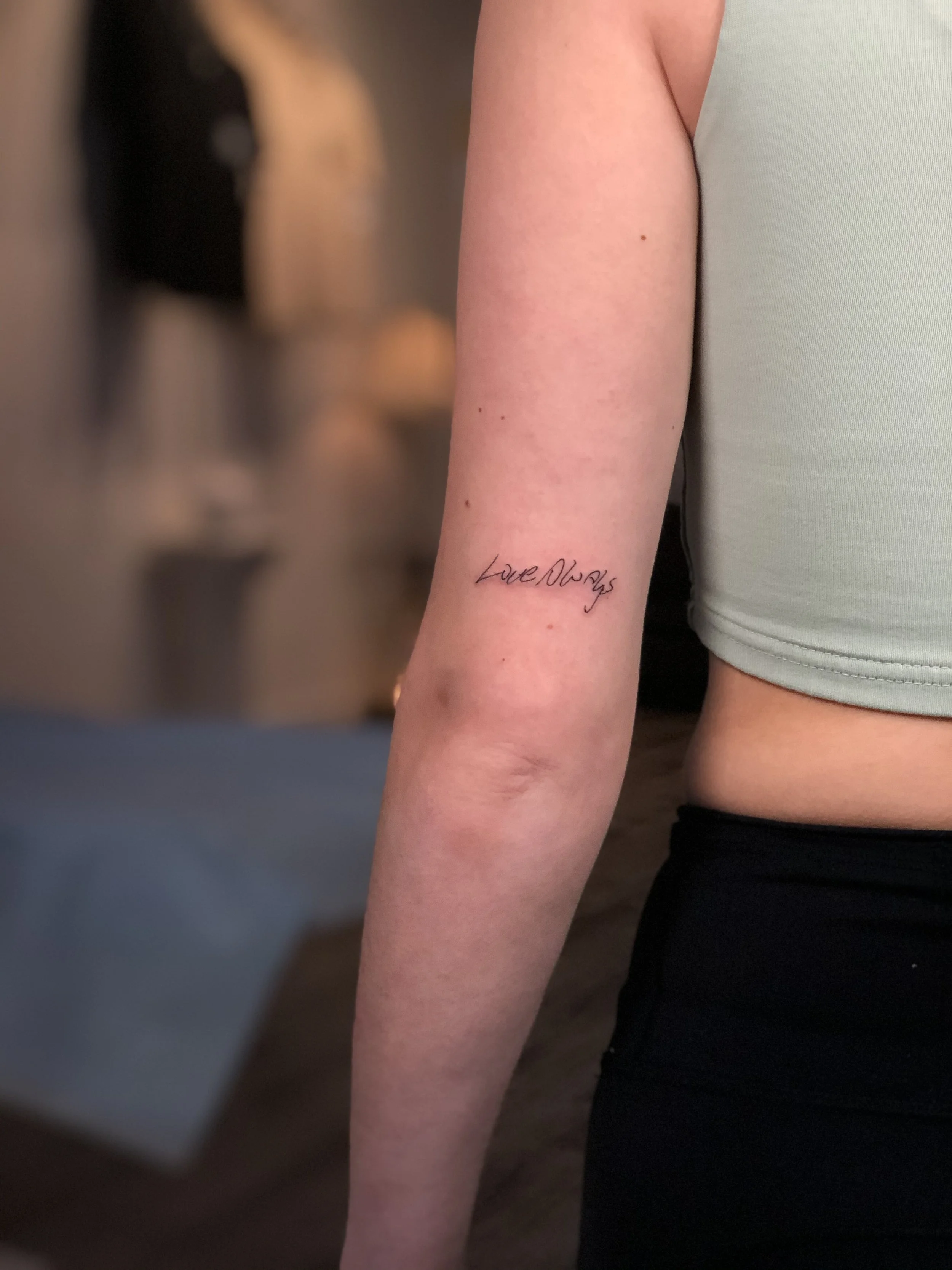 Close-up of a person's arm with a tattoo that reads 'Love Always' in cursive script.