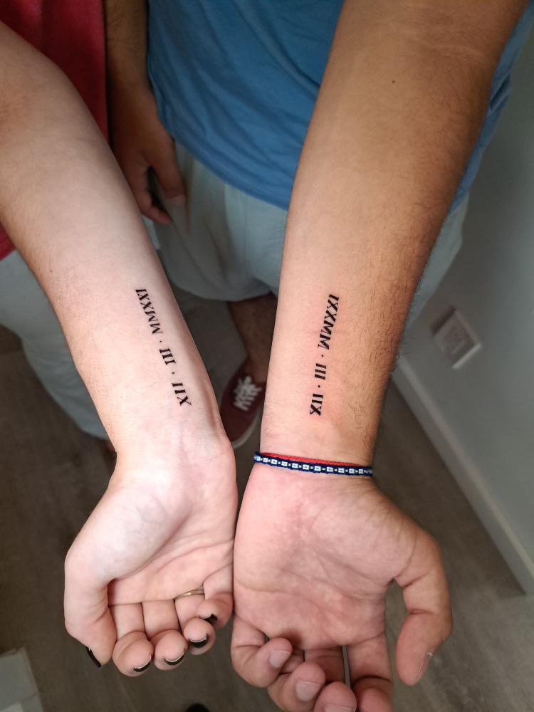 Two people holding hands with matching Roman numeral tattoos on their wrists.