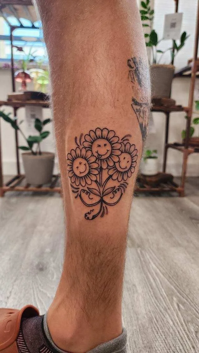 Tattoo of three smiling daisies with faces on the person's lower leg.