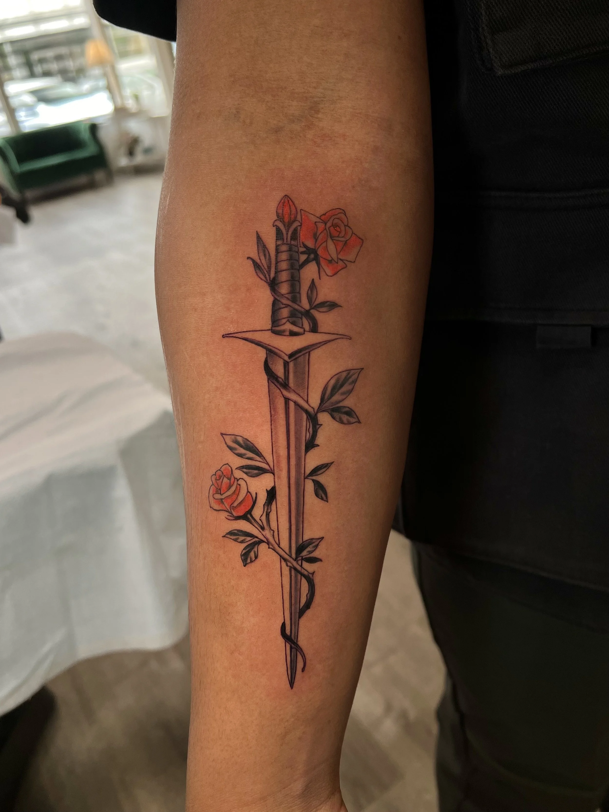 Tattoo of a sword intertwined with a rose and thorny vines on a person's arm.