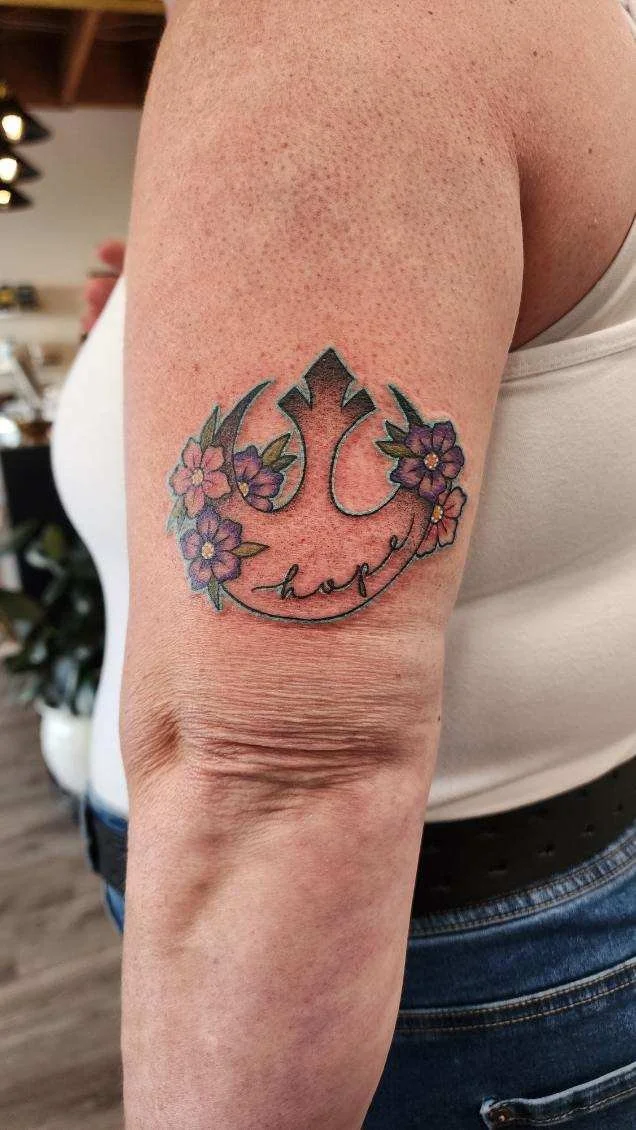 Tattoo of the Rebel Alliance symbol surrounded by purple flowers and the word 'hope' written in cursive.
