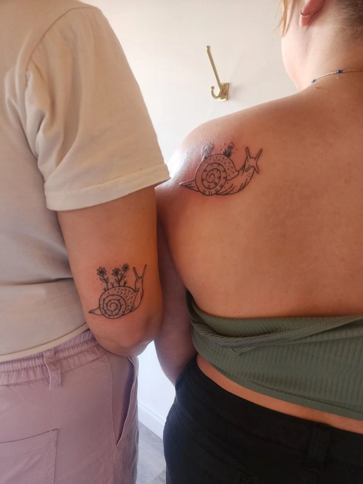 Two people with matching snail tattoos on their arms and shoulders.