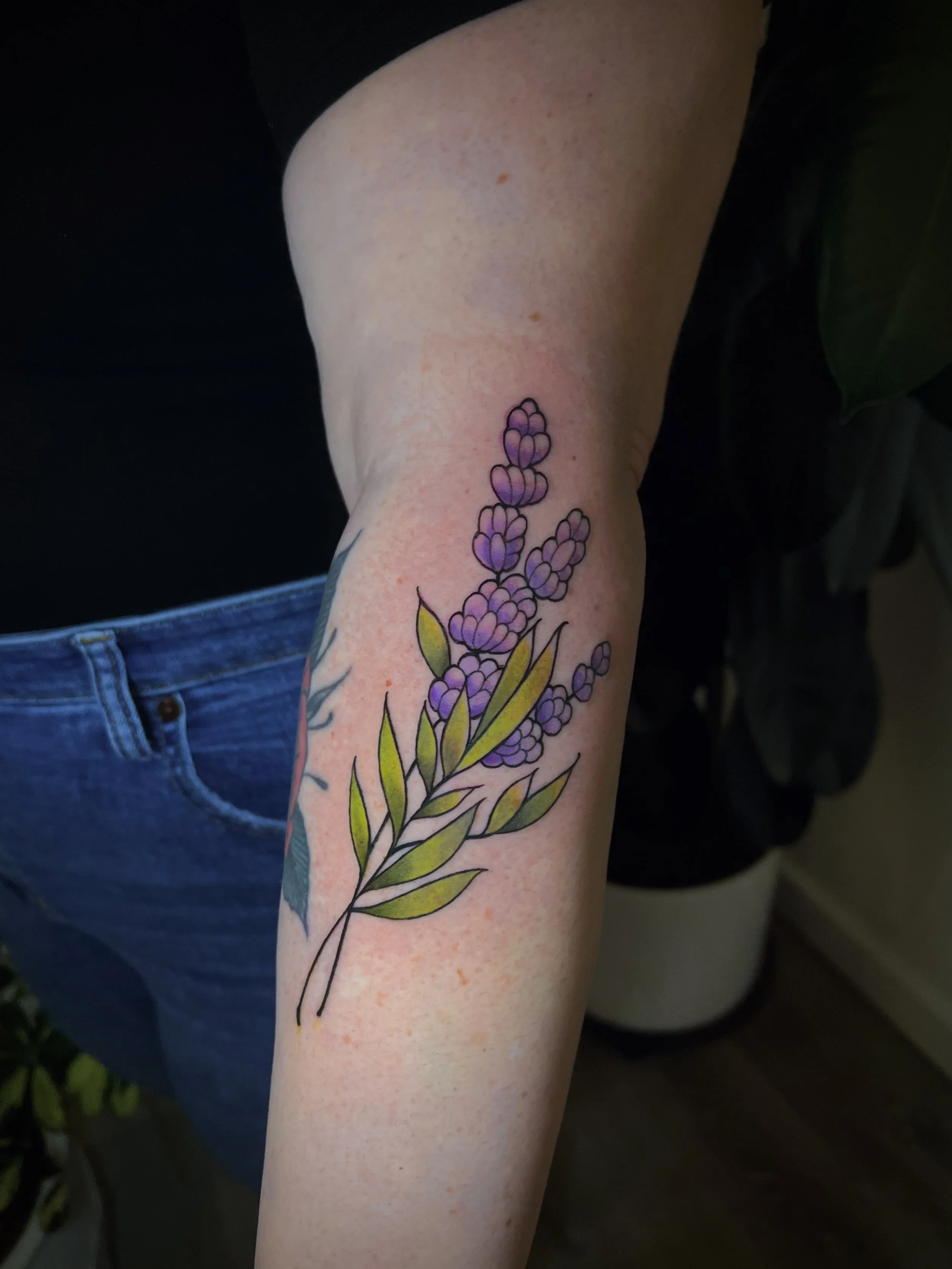 Colorful lavender flower tattoo on person's upper arm.