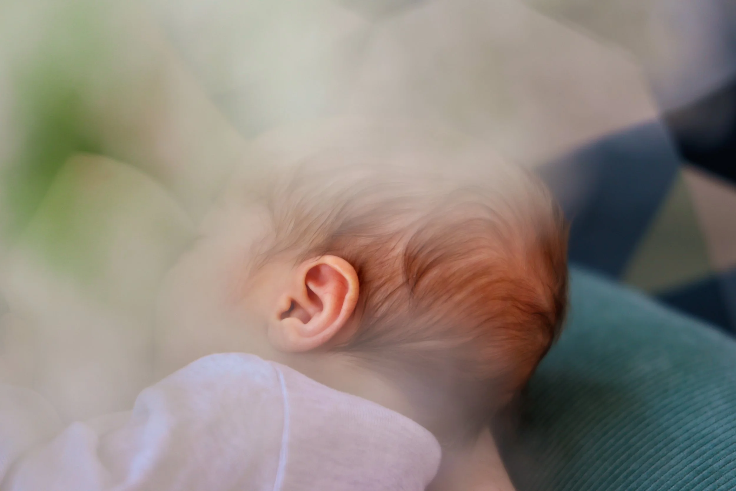 Nahaufnahme eines Babys mit rosiger Haut und großen Ohr, das auf der Seite liegt, gestillt wird.