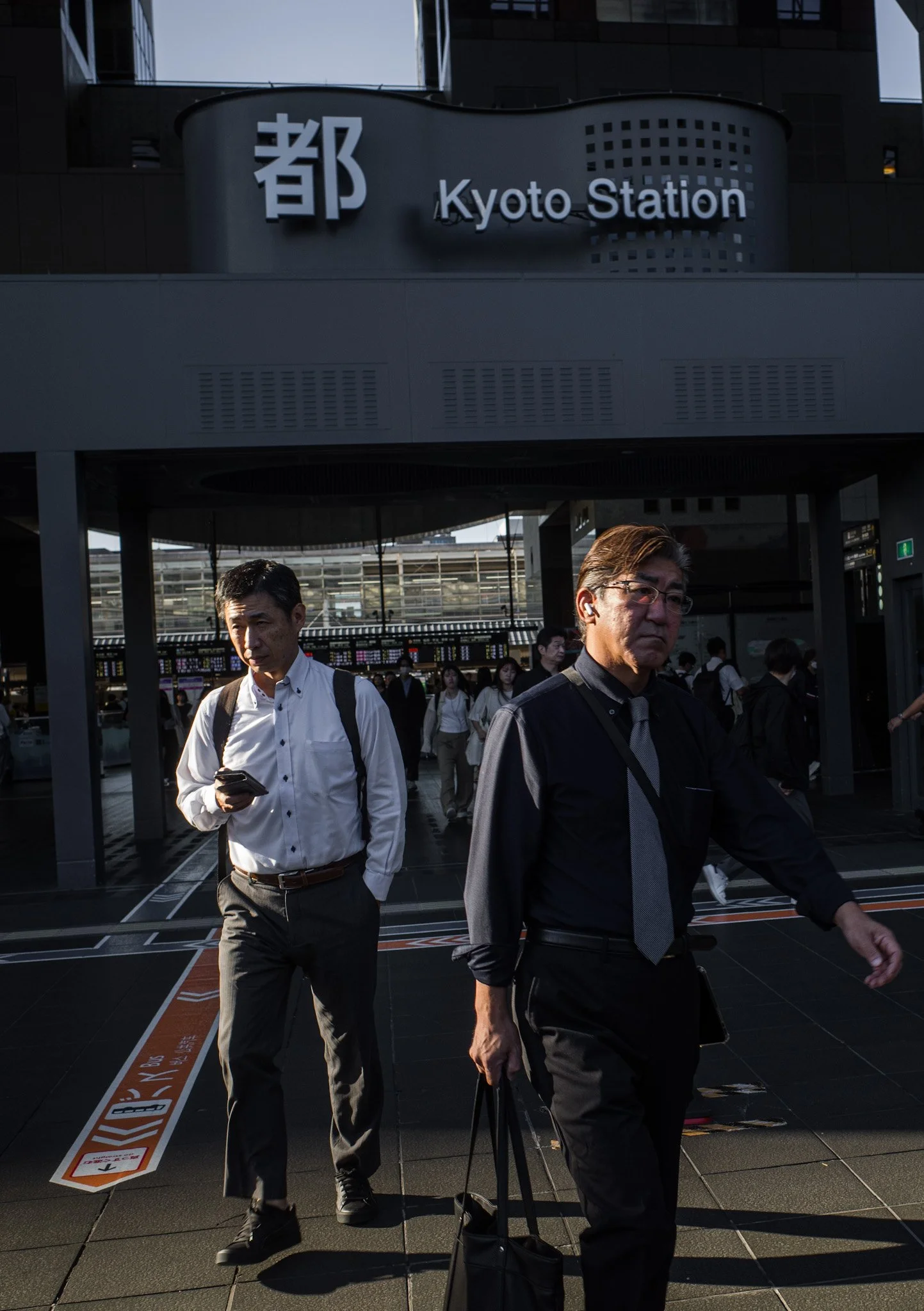 People walking out of Kyoto Station in Japan, with a sign displaying the station's name in English and Japanese characters in the background.