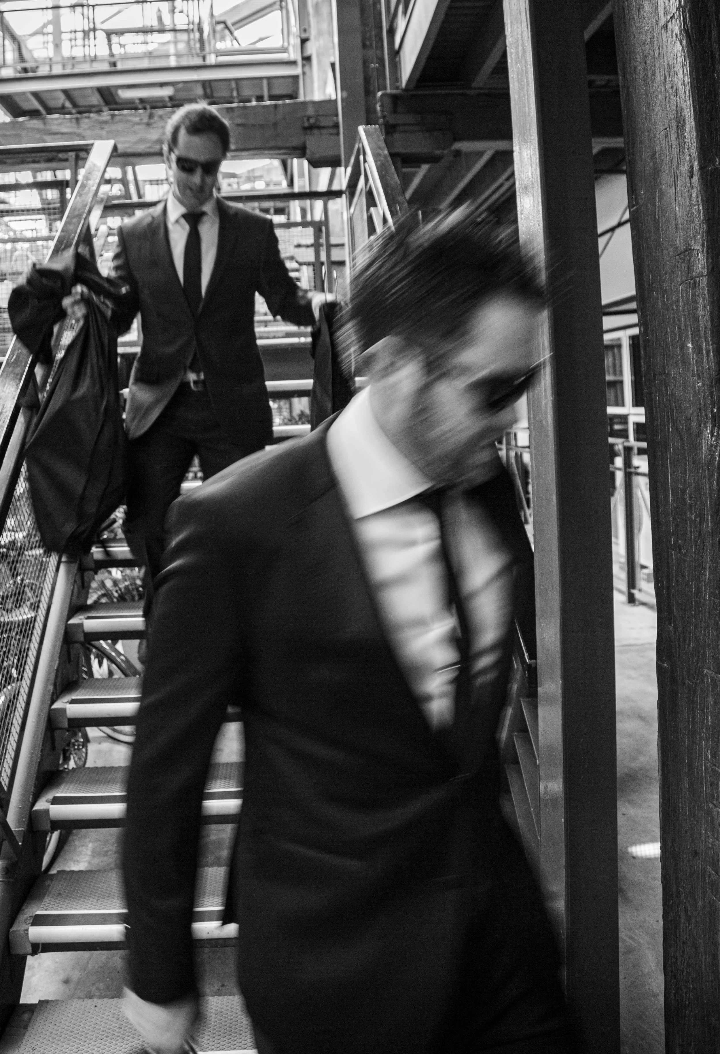 Two men in suits and sunglasses walking down a metal staircase, blurred motion.