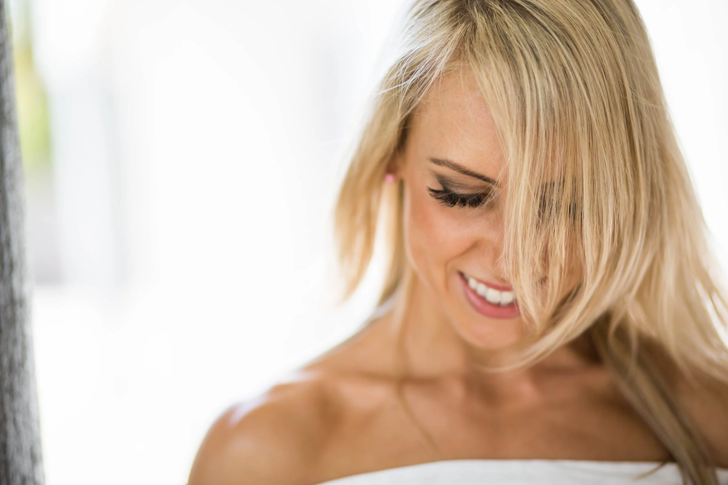 Close-up of a smiling blonde woman with styled hair and makeup, looking downward.