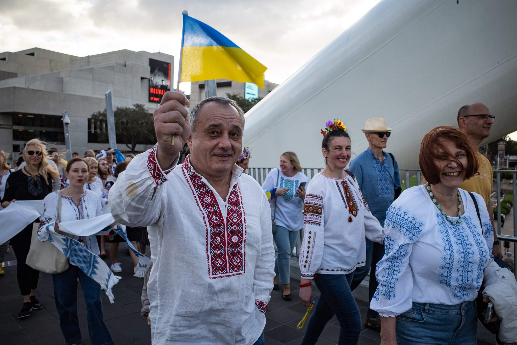 People participating in a parade or cultural event, wearing traditional embroidered clothing, with one person holding a Ukrainian flag.