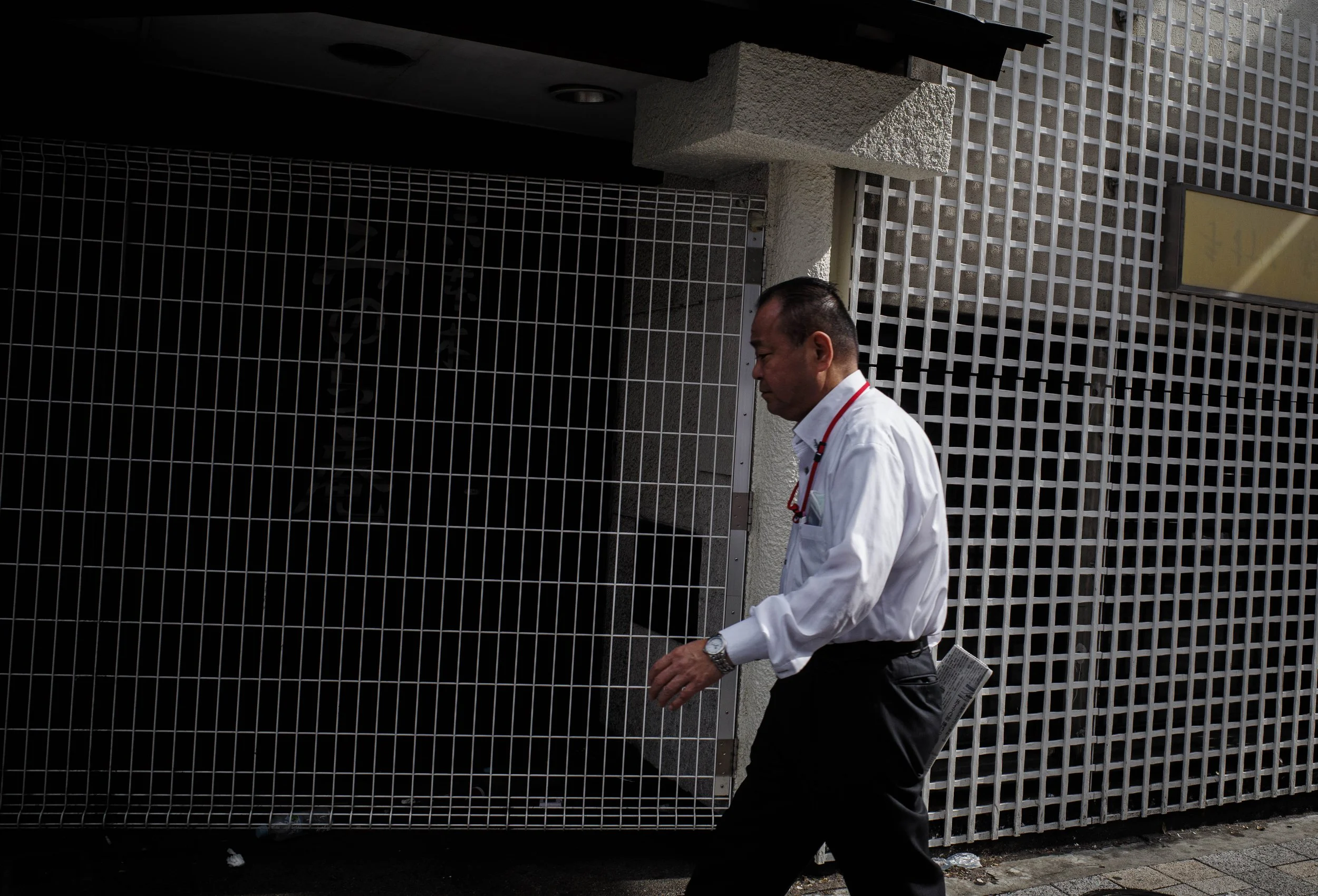 A man in a white shirt with a red lanyard walking past a building with a lattice metal facade.