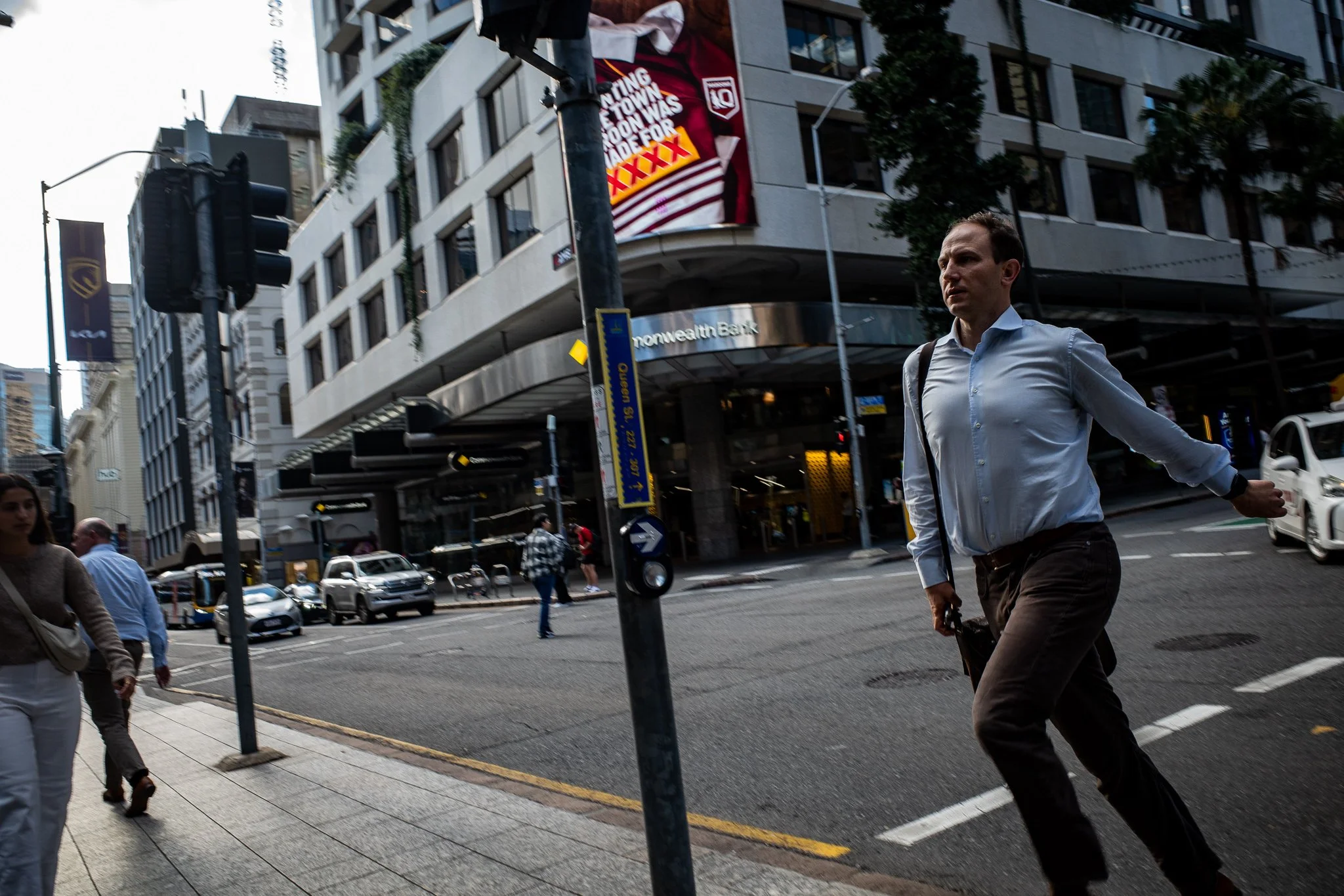 A man walking across a busy city street intersection with buildings, cars, and pedestrians around him.