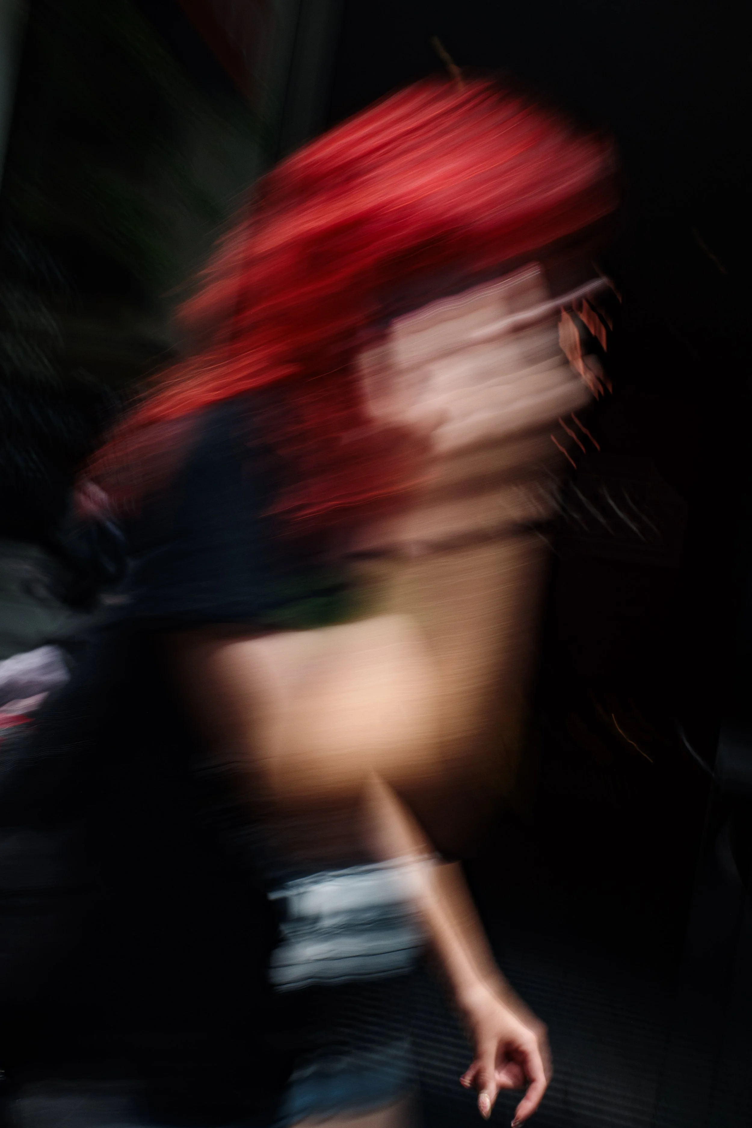 Blurry photo of a woman with red hair holding a phone, dressed in black, with a cardboard box in background.