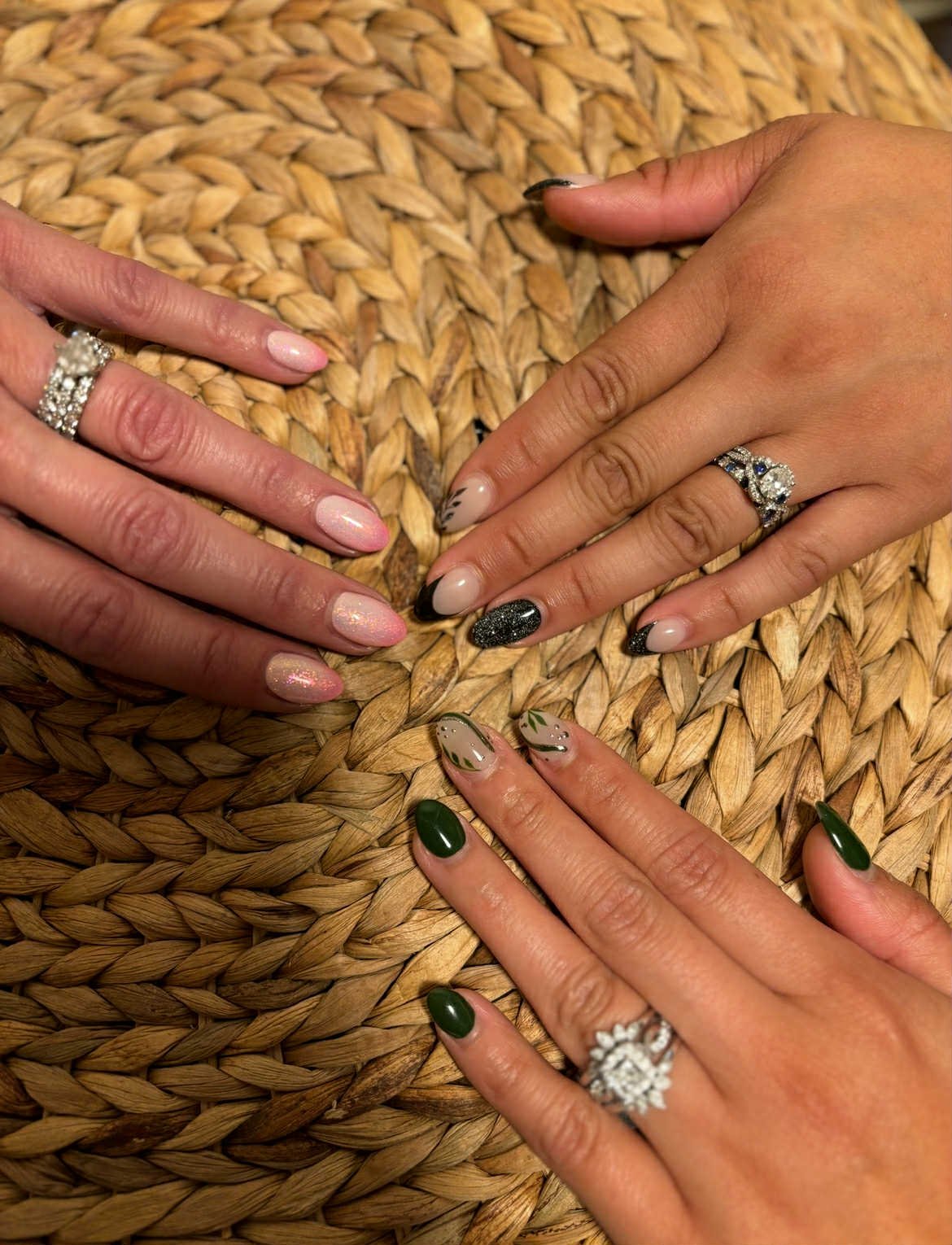 Three women displaying their manicured nails and rings on a woven surface.