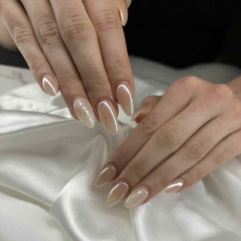 Close-up of hands with manicured nails in a nude and glitter design resting on white satin fabric.