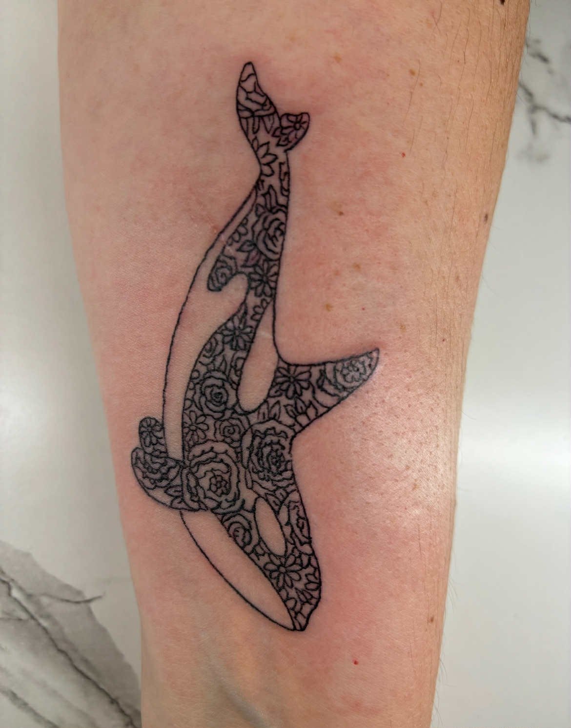 Tattoo of a whale outline filled with floral patterns on person's arm.