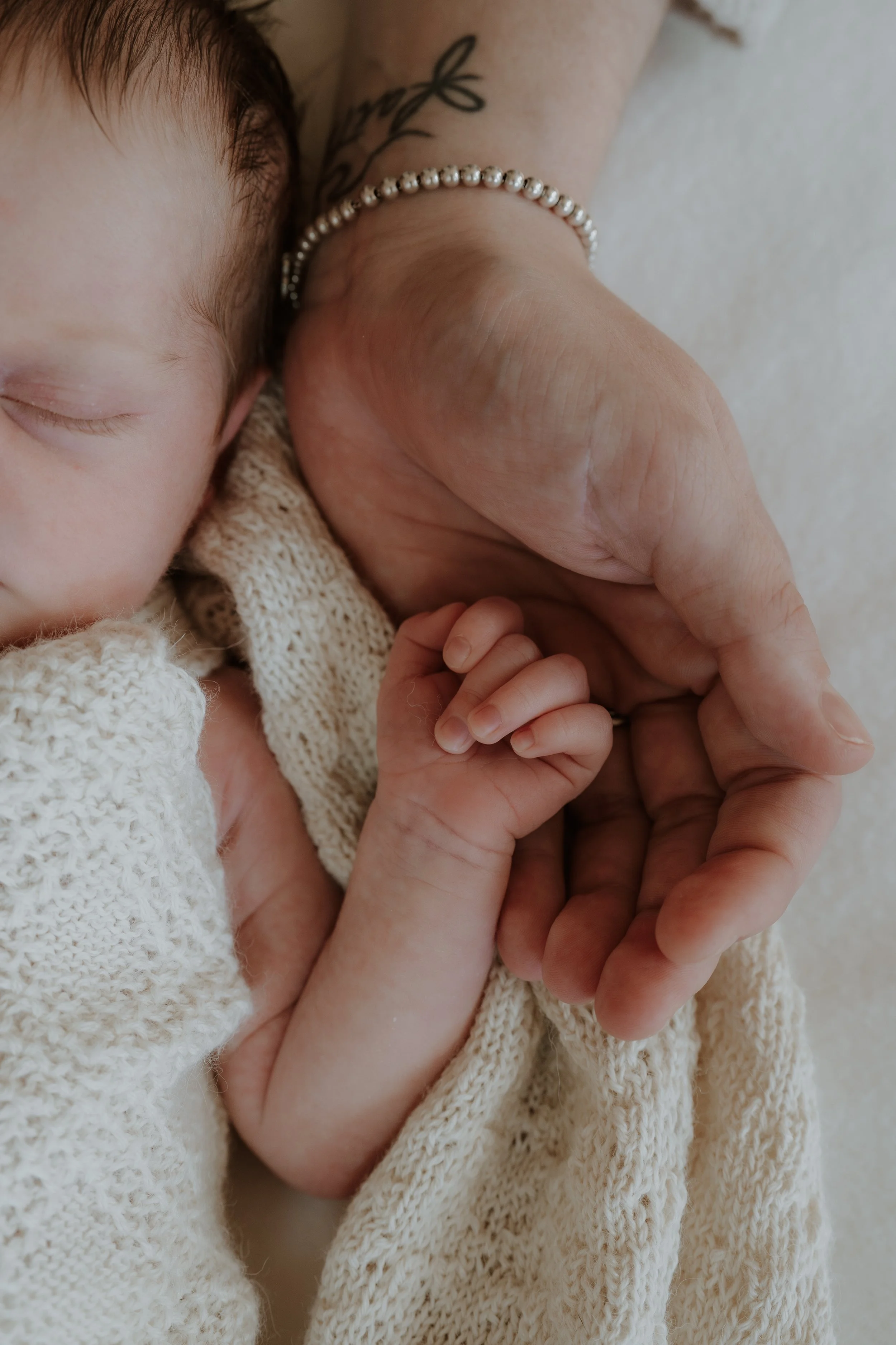 Close-up of a sleeping baby holding an adult's hand.