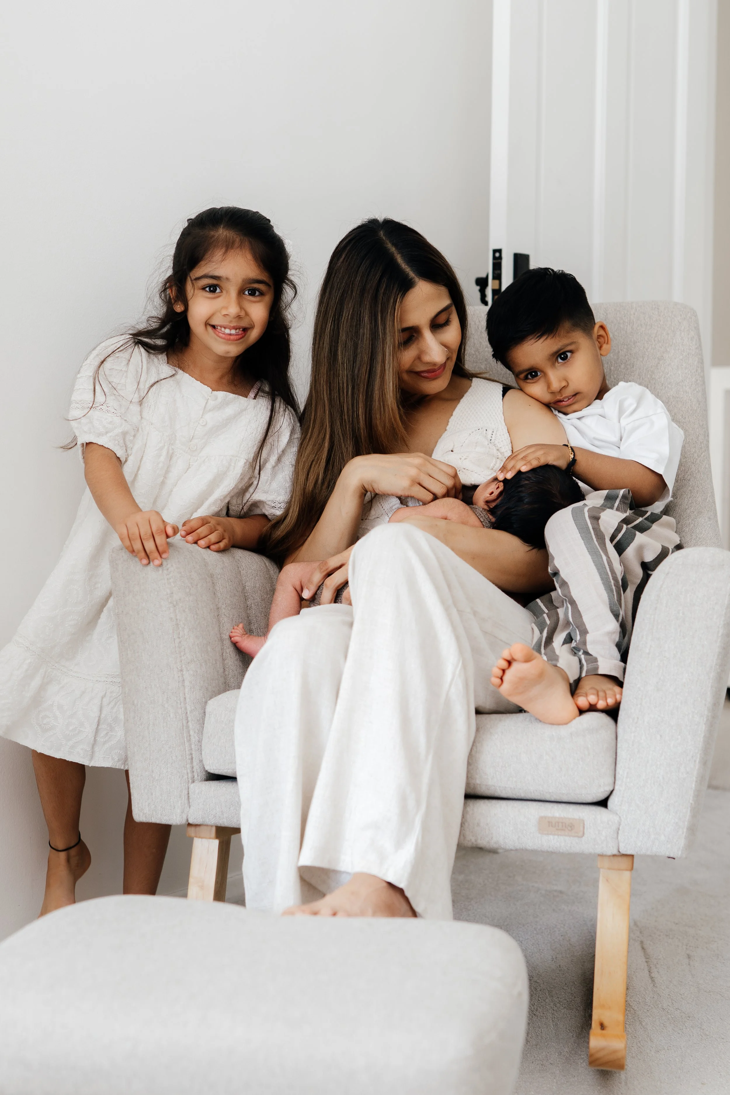 A woman cuddling her newborn with two children around her in a living room.