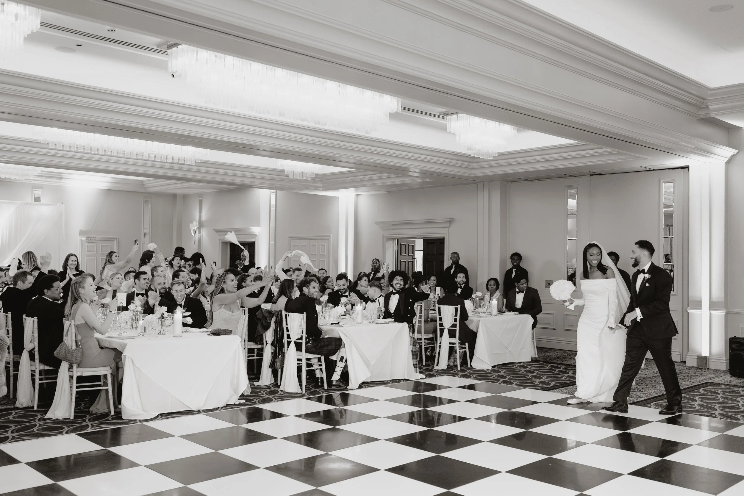 Bride and groom walking into their wedding reception with seated guests cheering and taking photos at Sopwell House.